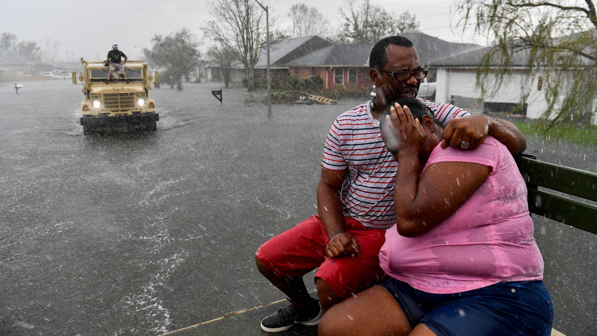 People react as a sudden rain shower soaks them with water while riding out of a flooded neighborhood of LaPlace, La.