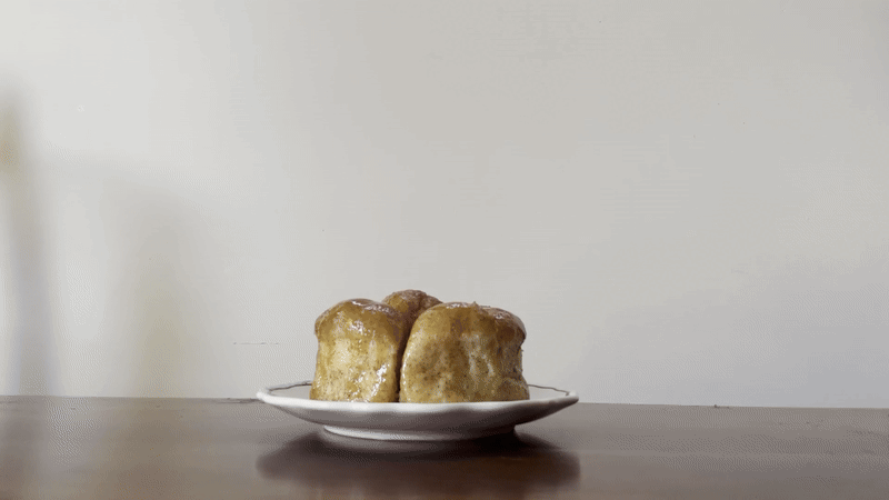A plate of rolls sits on a table as a pair of hands pulls one of the rolls apart.