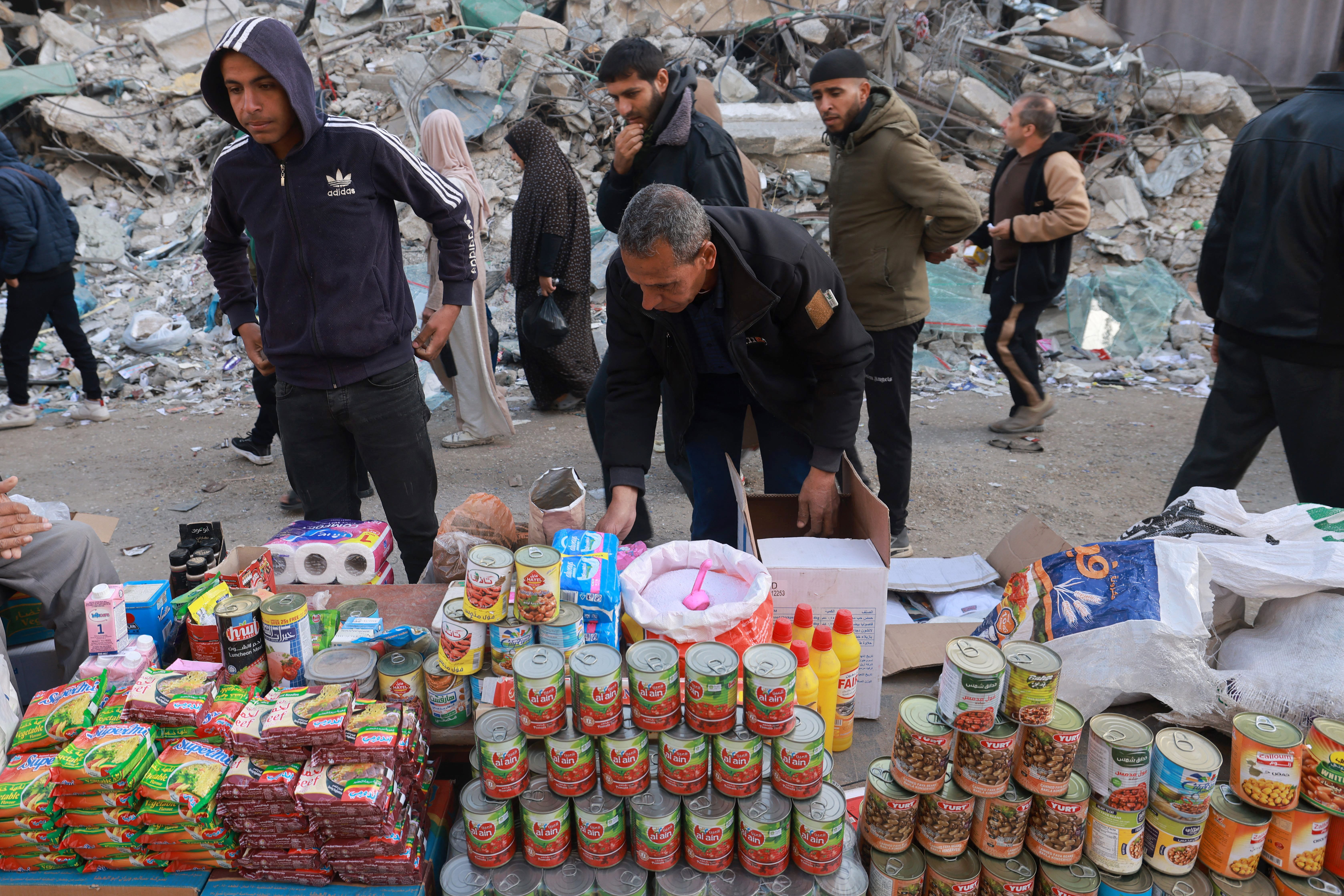Palestinians walk past make-shift dry goods stalls set up on a street.