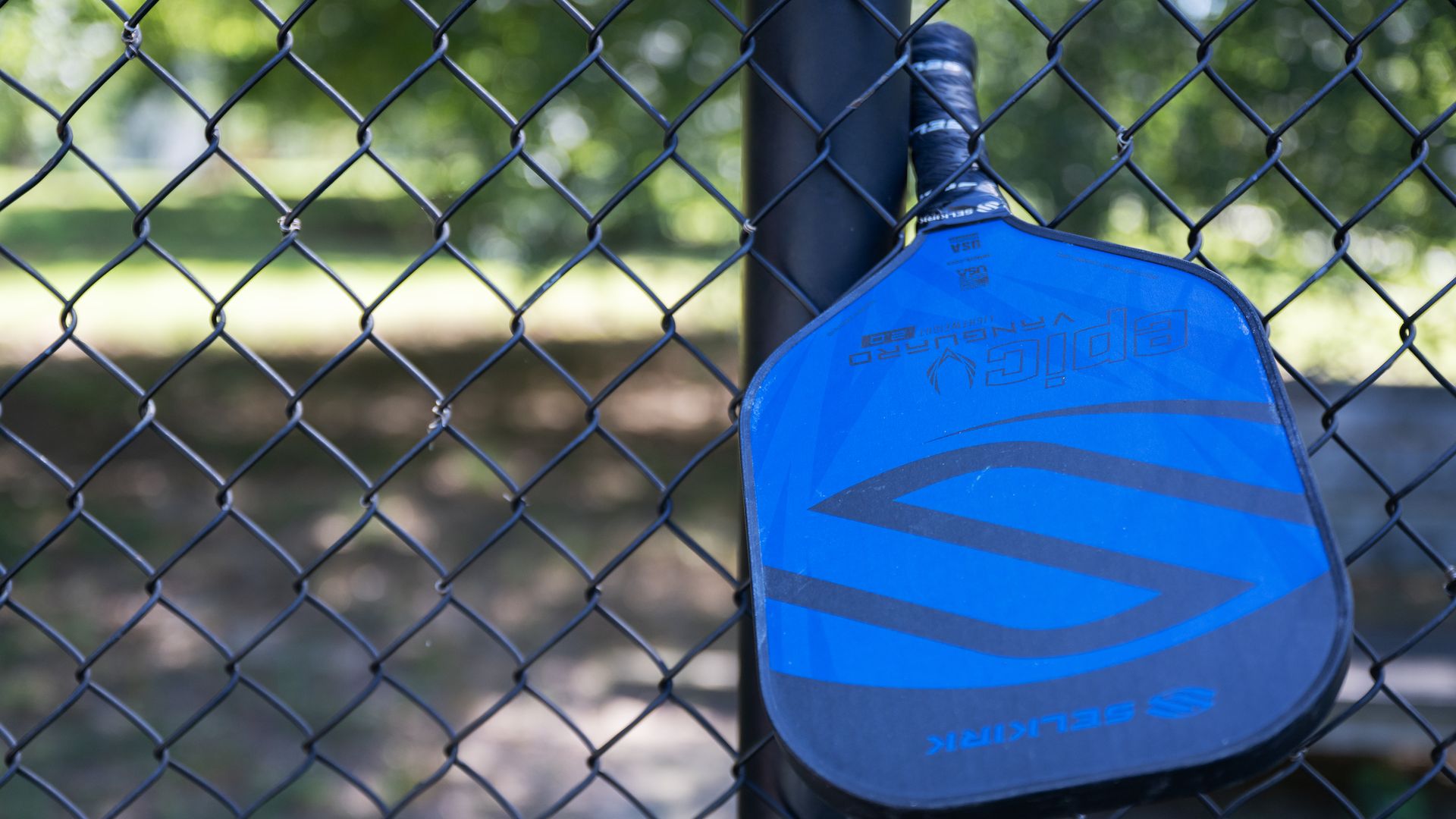 An image of a pickleball paddle hanging from a pickleball court fence. 