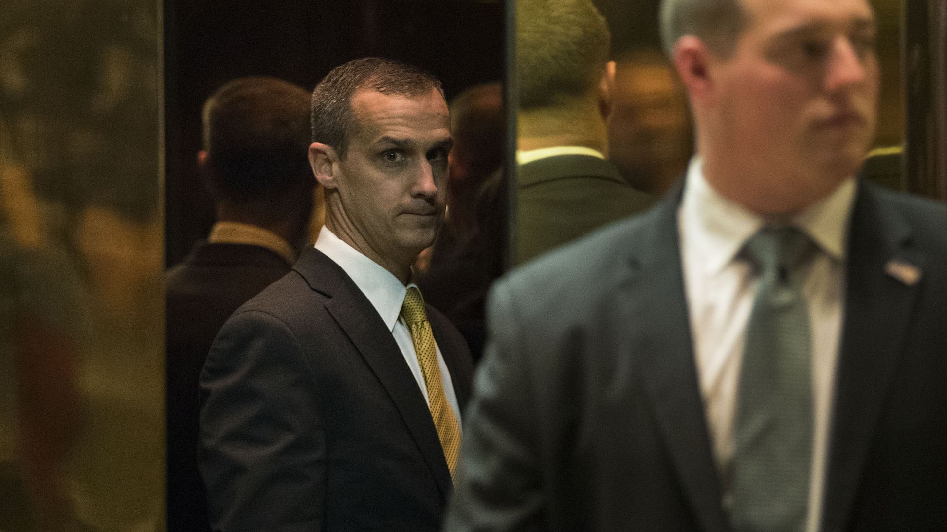 Corey Lewandowski seen between gold elevator doors looks disconcerted. 