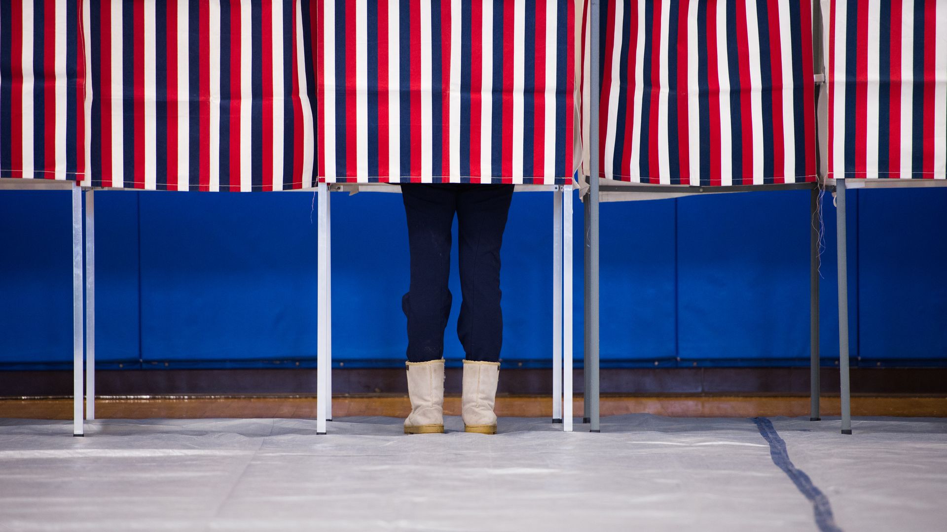 Pair of feet in blue pants underneath polling booth with red, white, blue stripes.