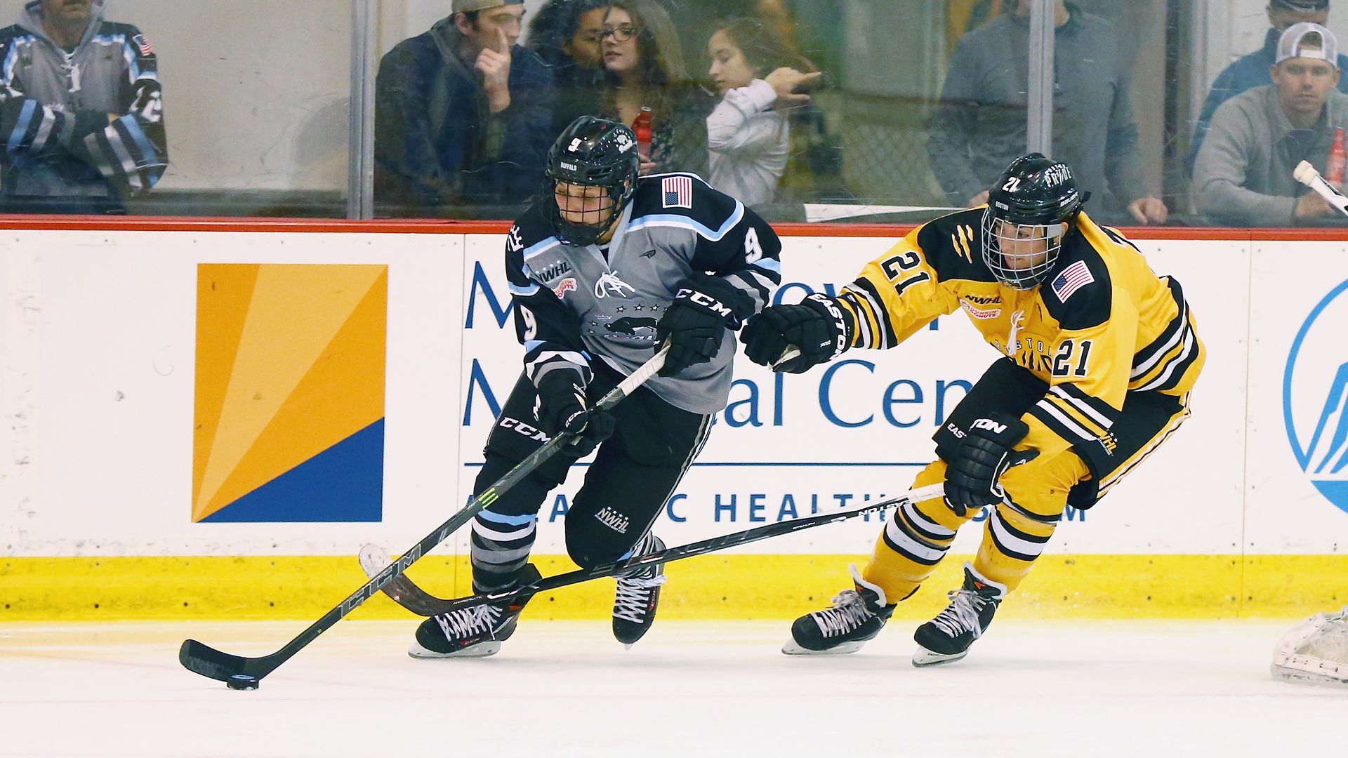 Megan Bozek #9 of the Buffalo Beauts plays the puck while being defended by Hilary Knight #21