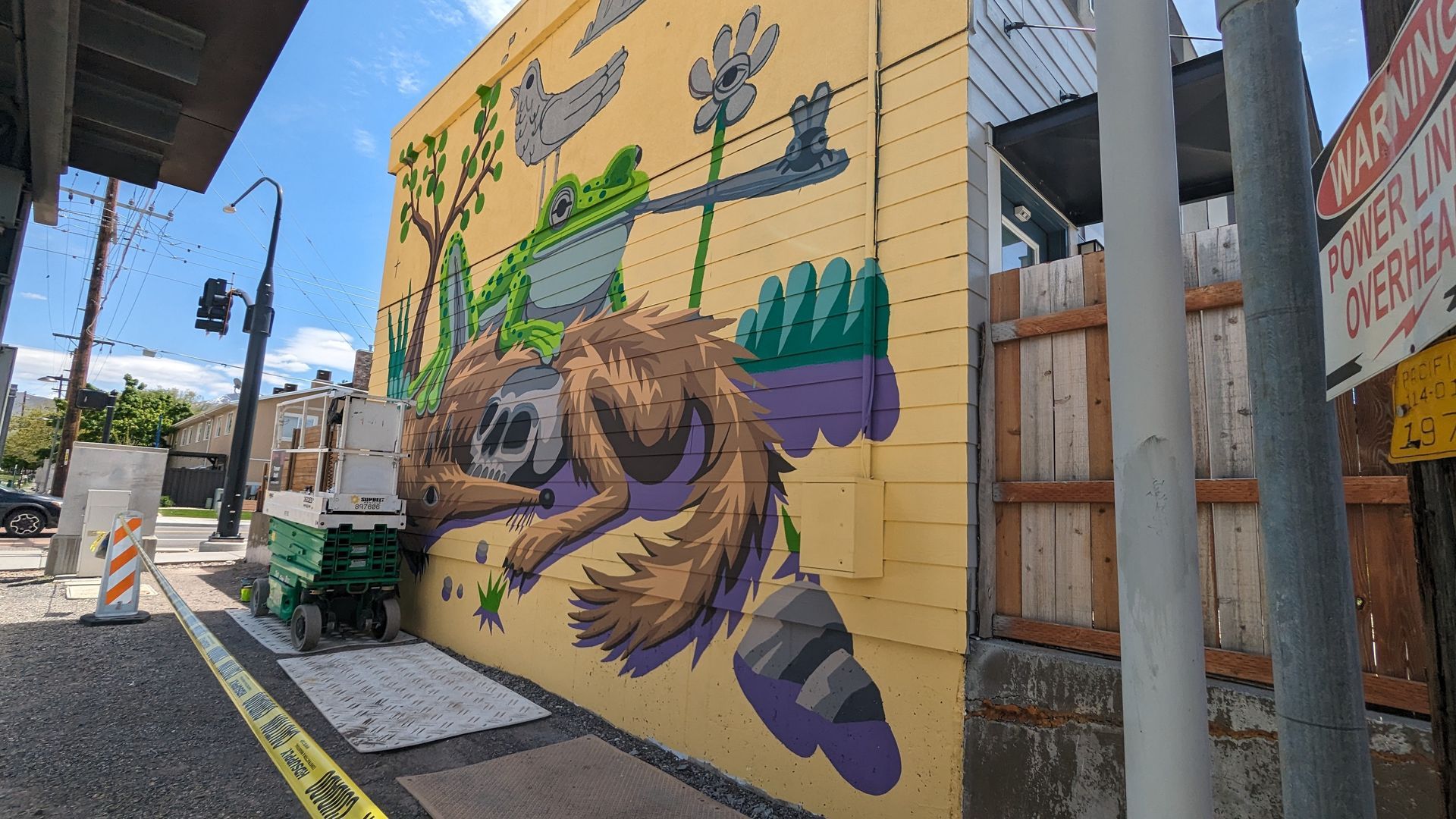 A mural on a yellow wall feature purple and green colors and a frog 