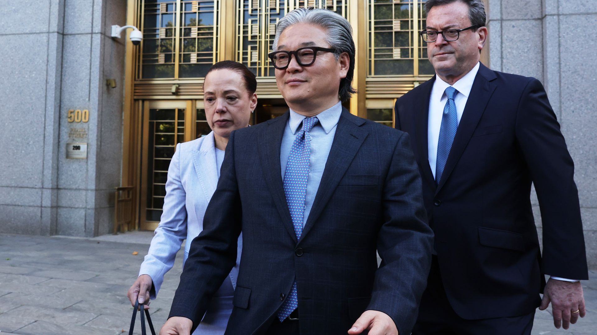 two men in suits and a woman walking out of a Manhattan courthouse