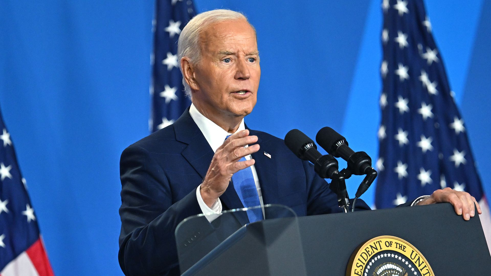 President Biden, wearing a blue suit and speaking at a podium.