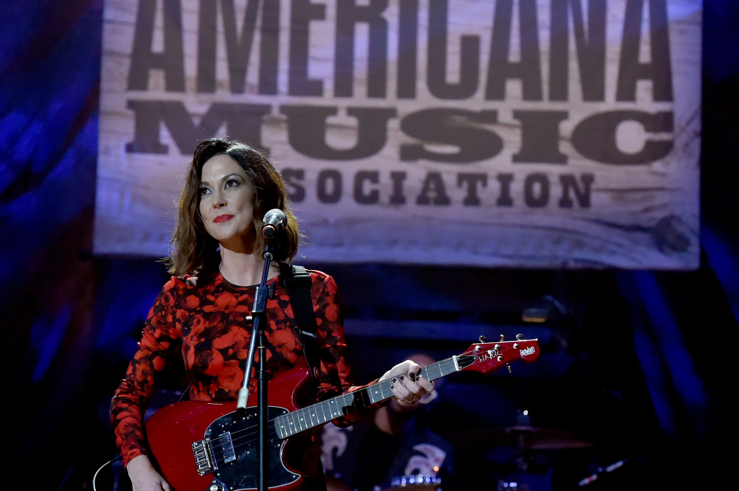 Shires in a red dress, playing a big red guitar.