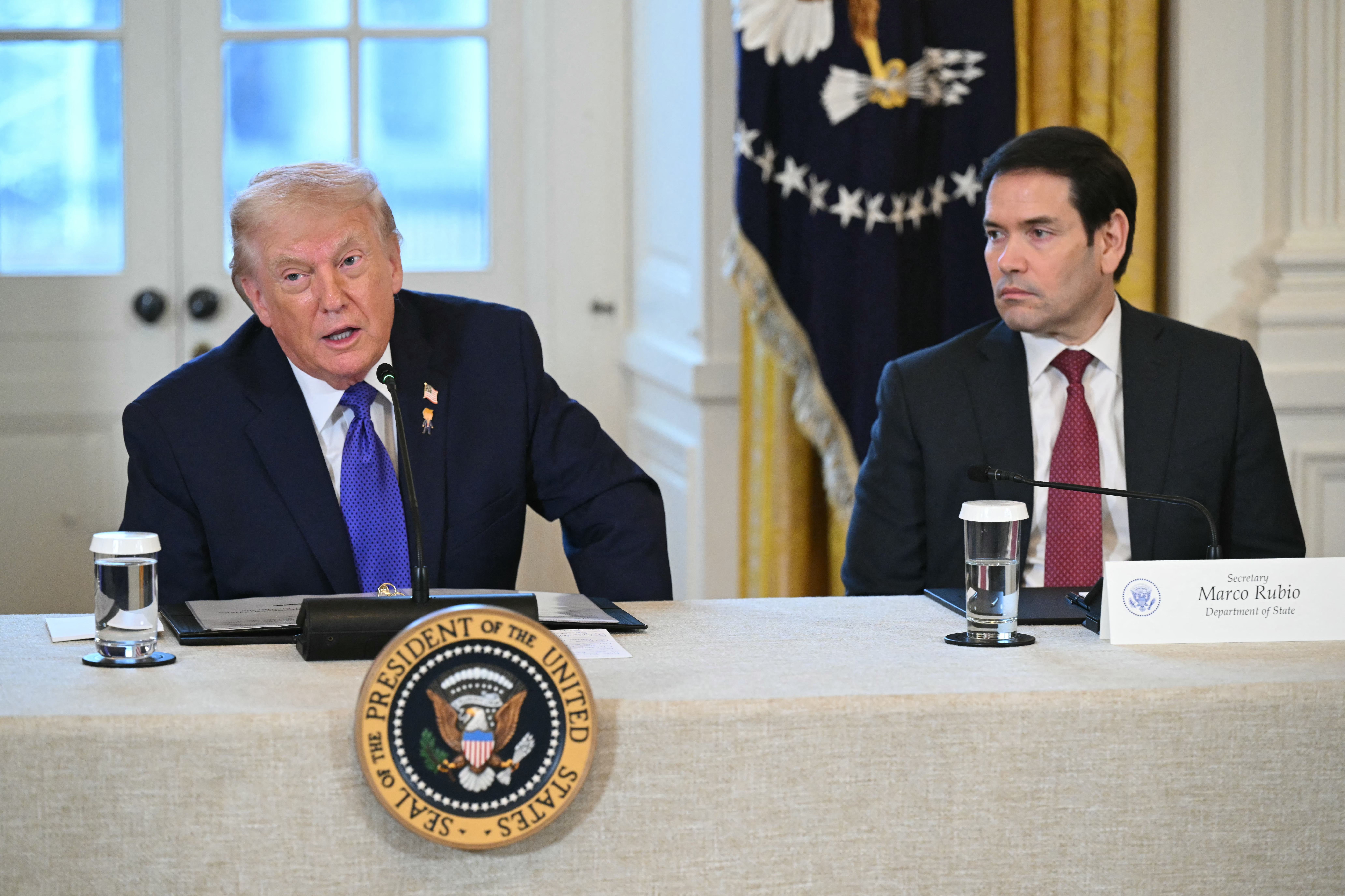 President Donald Trump at a podium in the White House East Room addressing U.S. oil company executives, with Secretary of State Marco Rubio standing to his right.