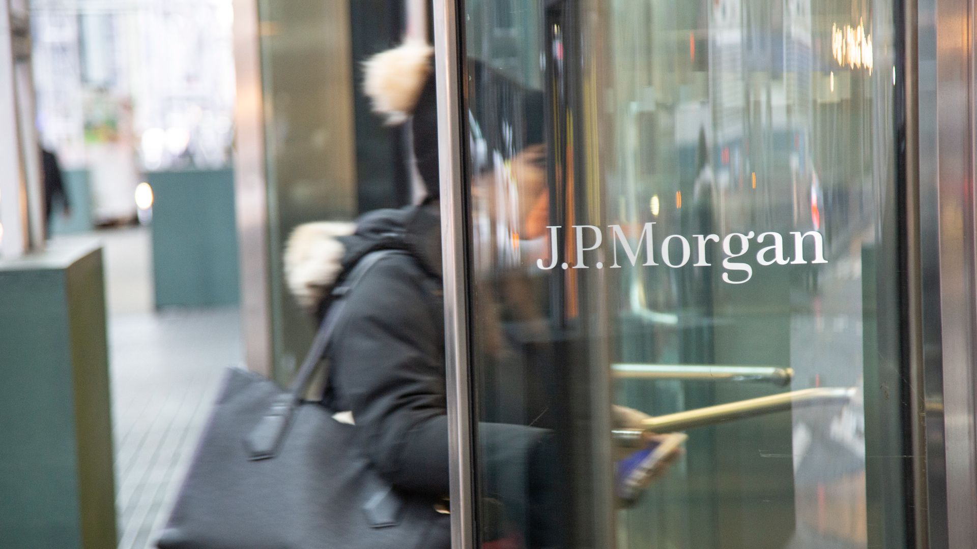 Photo of a masked person entering a glass revolving door that shows the JPMorgan logo 