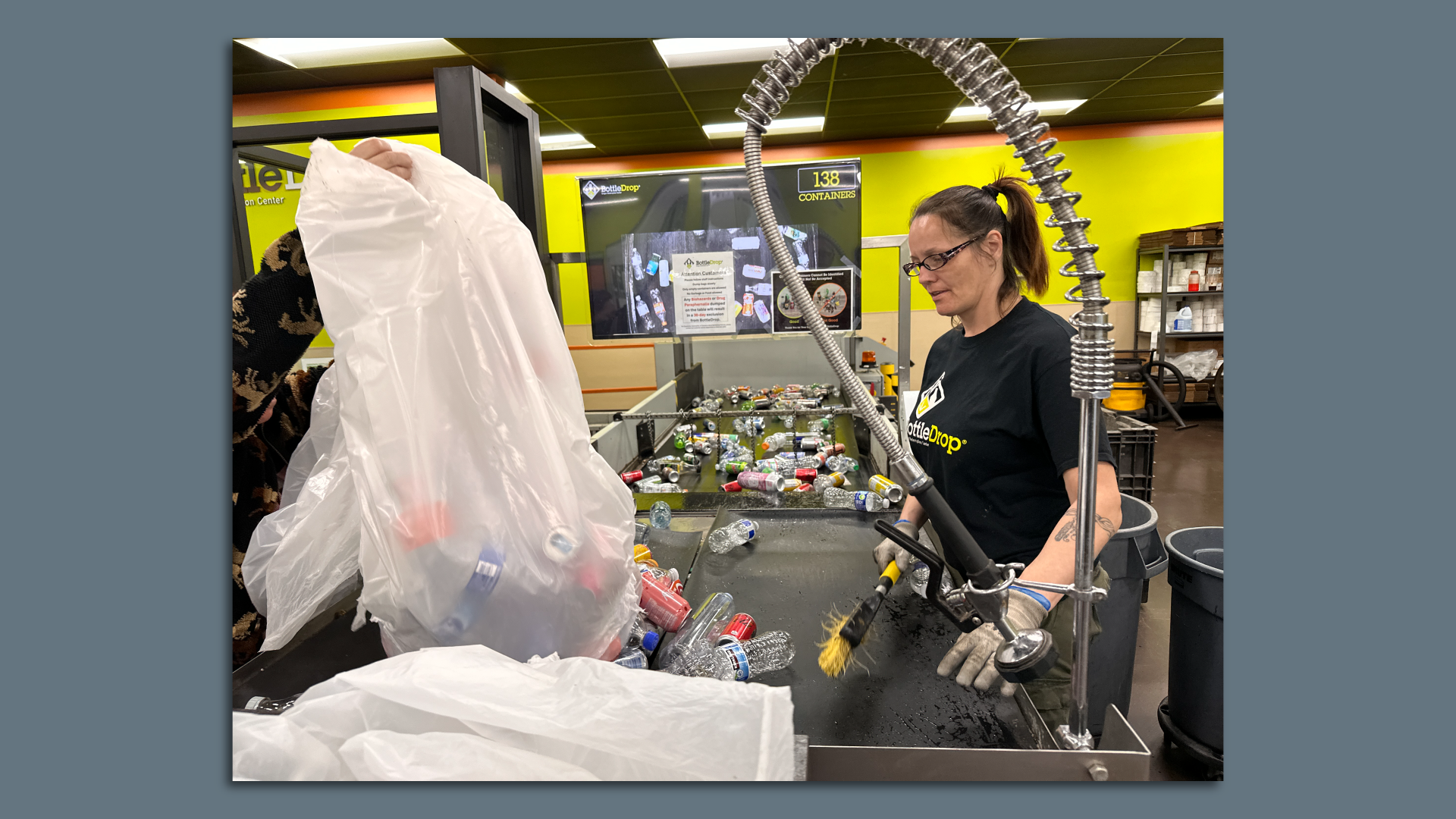 A worker at the NE122nd Ave bottle drop helps bottles and can along a conveyor belt.  