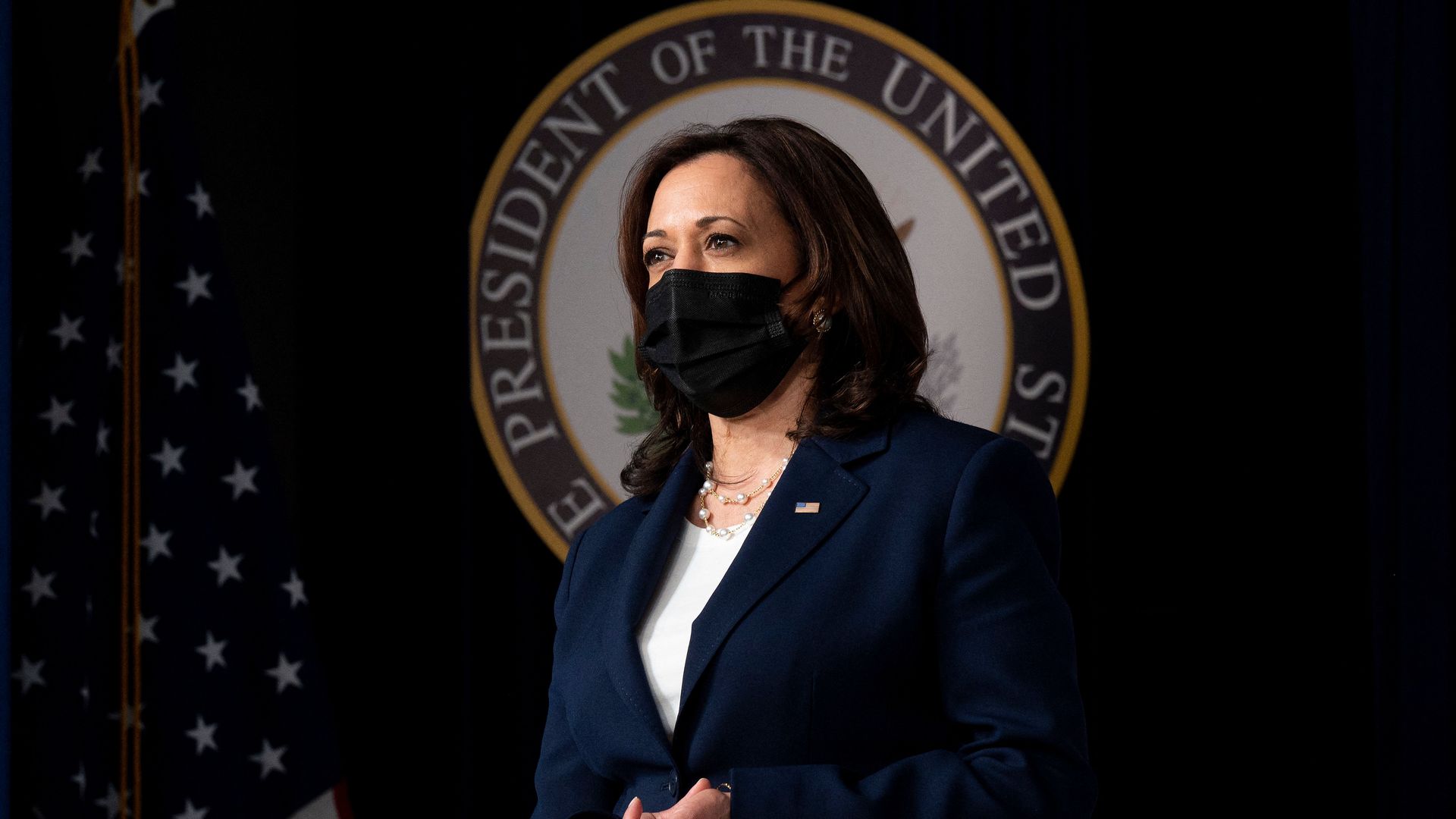 Kamala Harris stands on a stage wearing a black mask