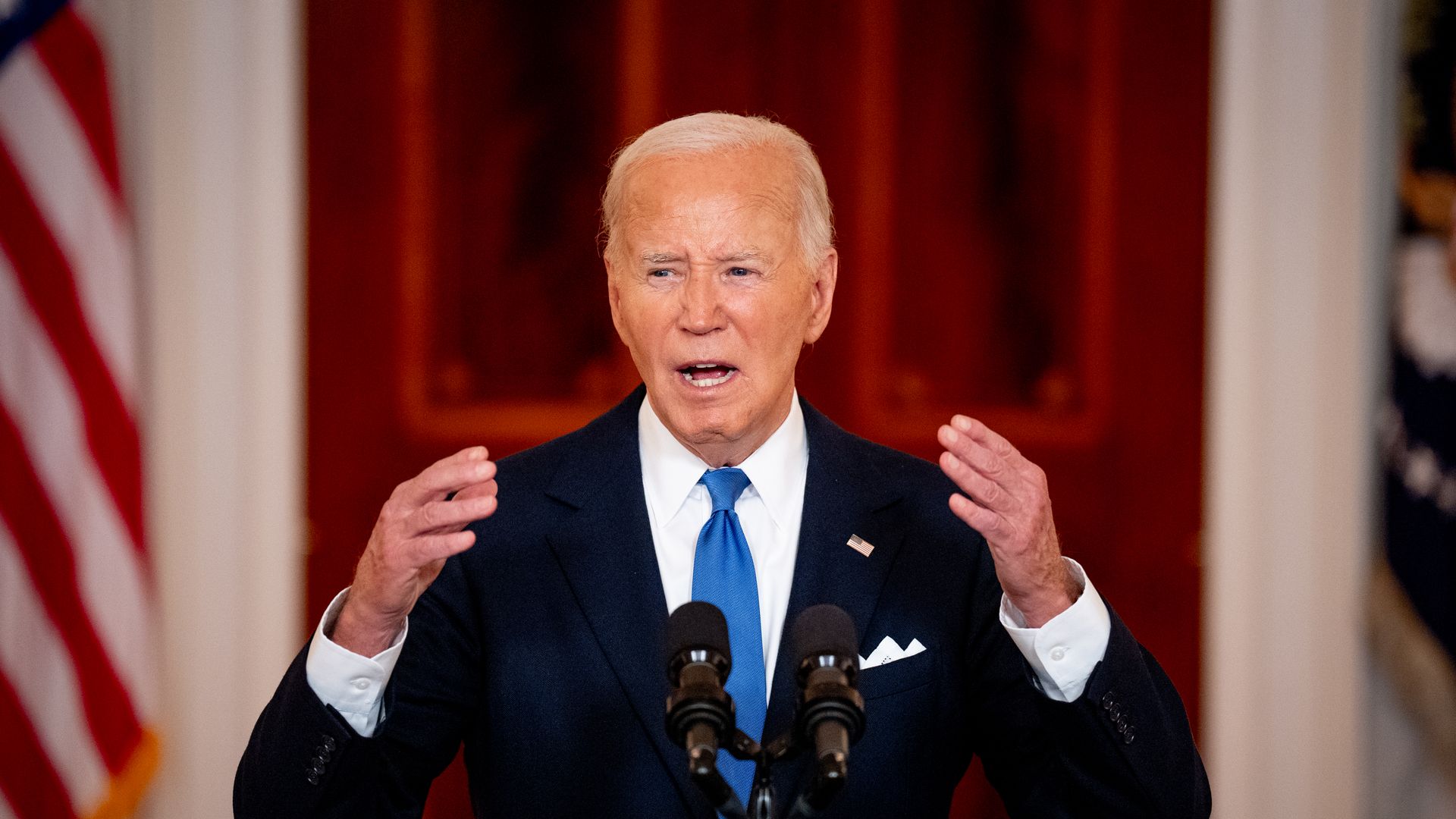 President Biden speaks in a dark suit, white shirt, blue tie.