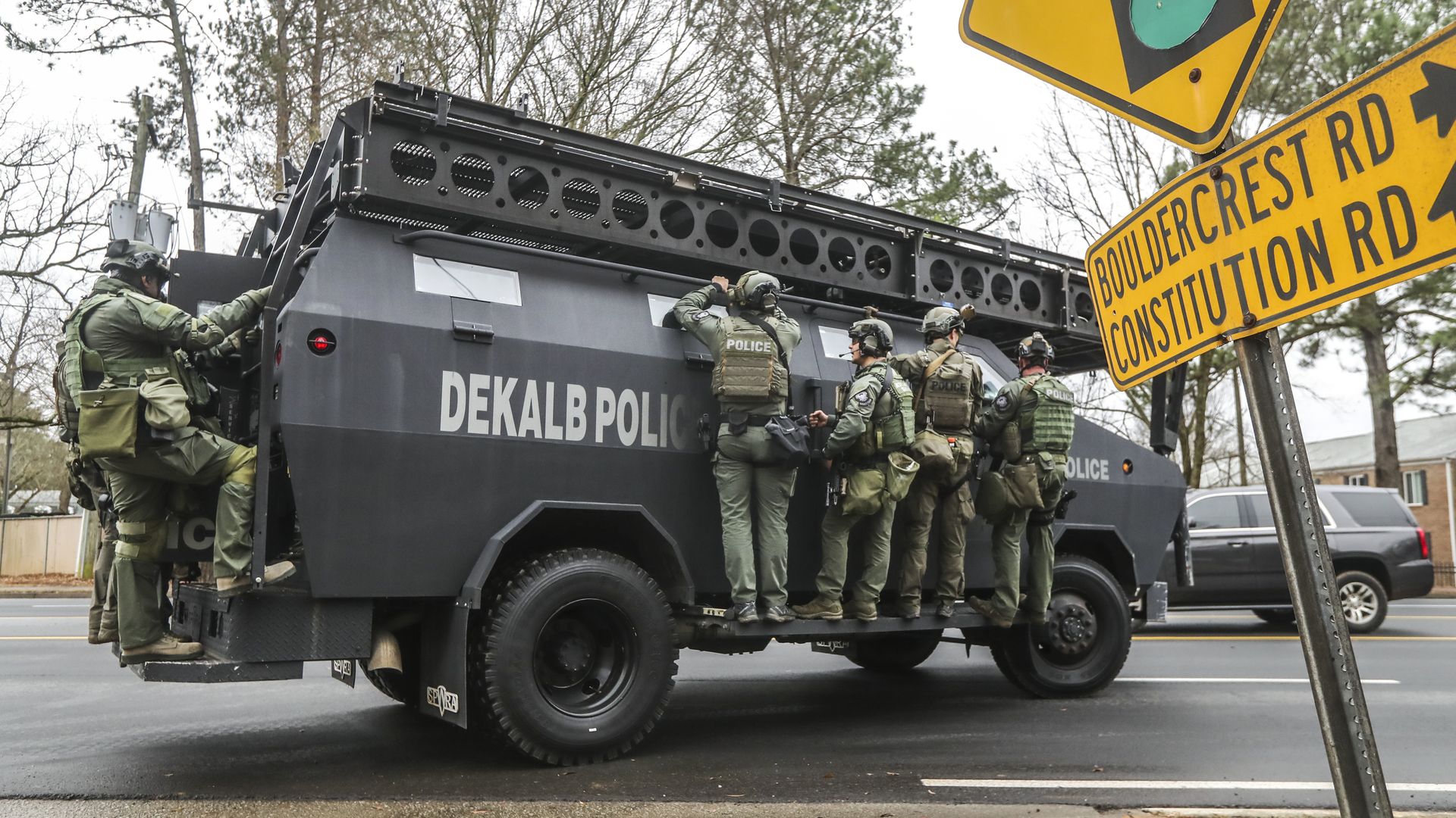 Police officers in tactical and protective gear hang on to the side of a SWAT truck