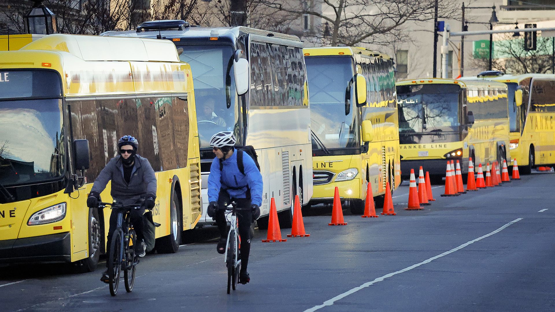 Cyclists ride in Kenmore Square near a line of shuttle buses parked and closed off with traffic cones during a Green Line closure in 2024 .