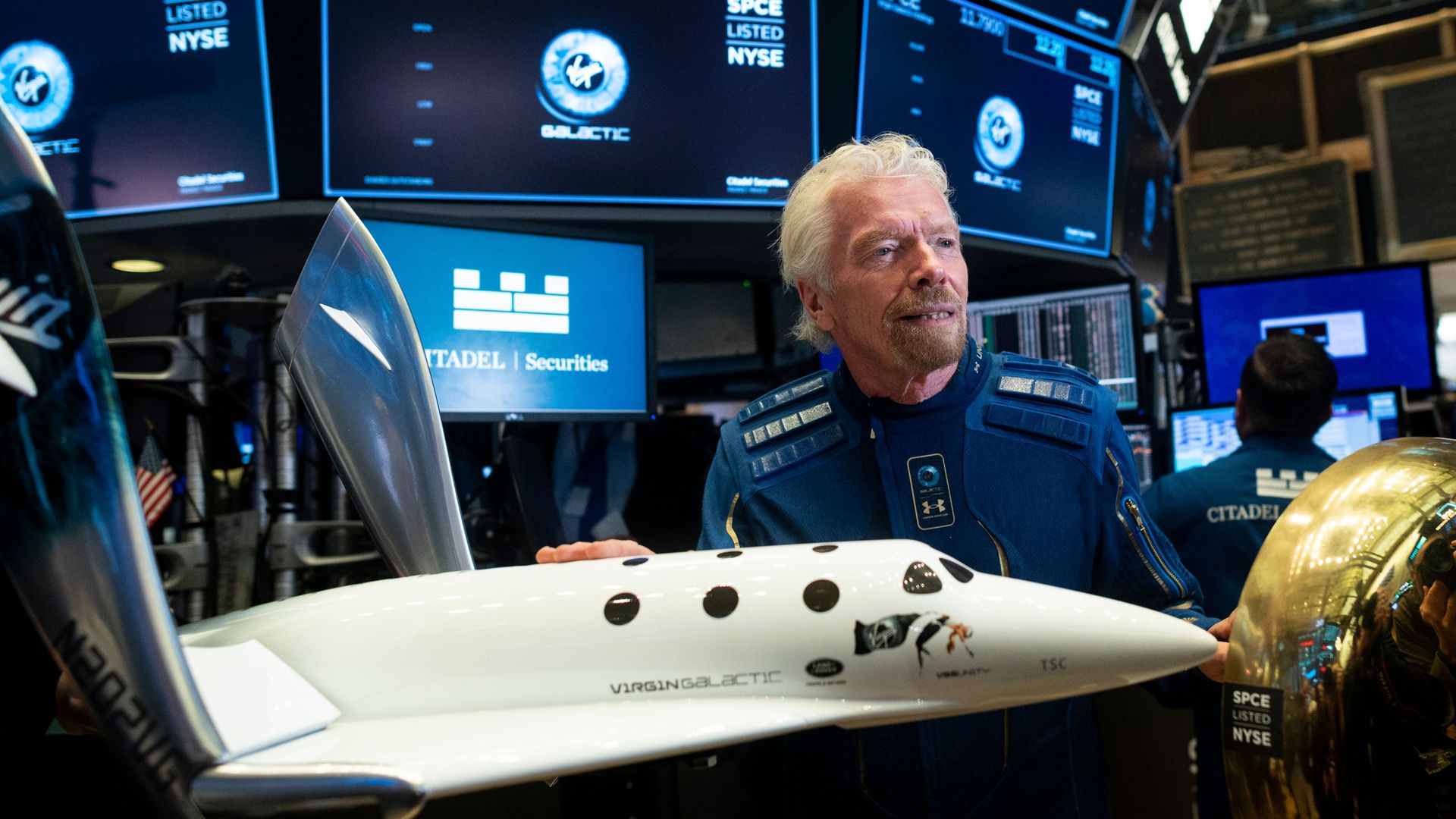 Richard Branson, founder of Virgin Galactic, posing with a model of VSS Unity on the floor of the New York Stock Exchange in October 2019. 