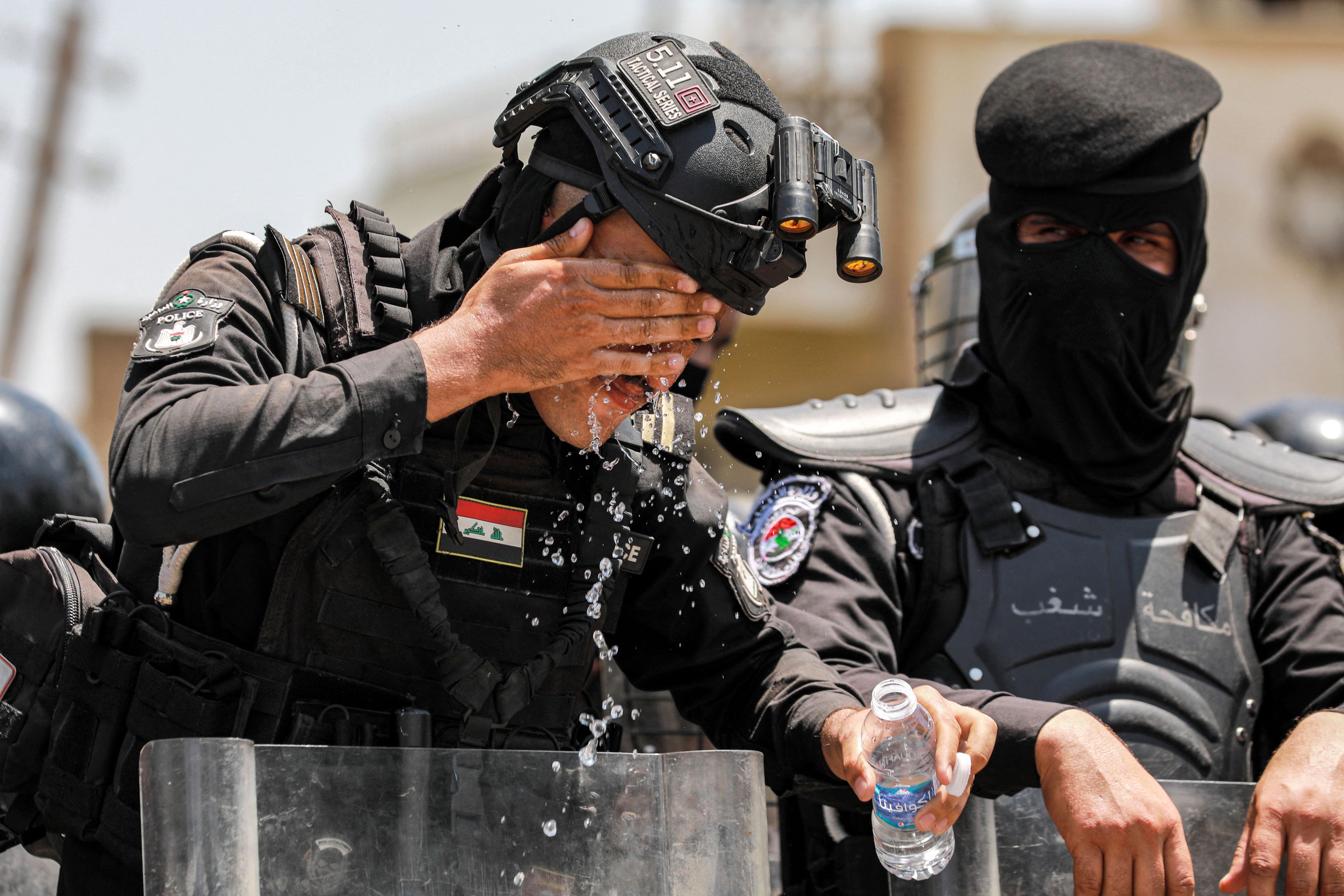 An Iraqi security forces member standing guard at a demonstration against water scarcity and power outages rinses his face with water from a bottle to cool off in Baghdad on July 18, 2023 during a heat wave. Designated by the United Nations as one of the five countries in the world most touched by some effects of climate change, Iraq is experiencing its fourth consecutive summer of drought. In addition to declining rainfall and rising temperatures, Iraqi authorities say upstream dam construction by Turkey and Iran has affected the volume of water in the Tigris and Euphrates rivers through Iraq. 
