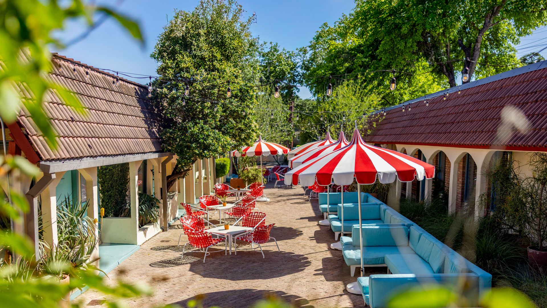 A photo of a courtyard with red and white umbrellas and blue chairs.