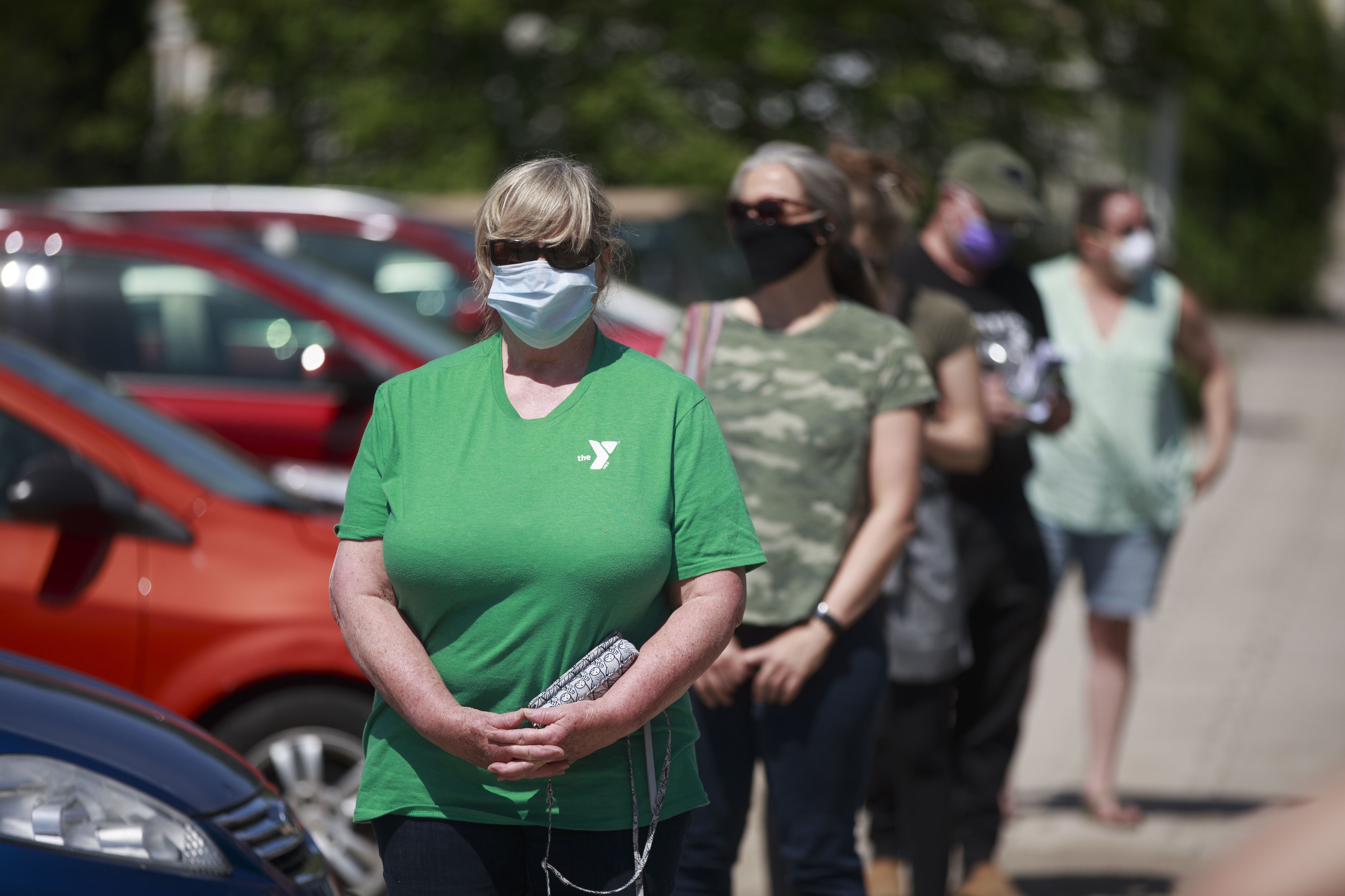 A woman stands at the front of a line of voters in a parking lot. All are wearing face masks