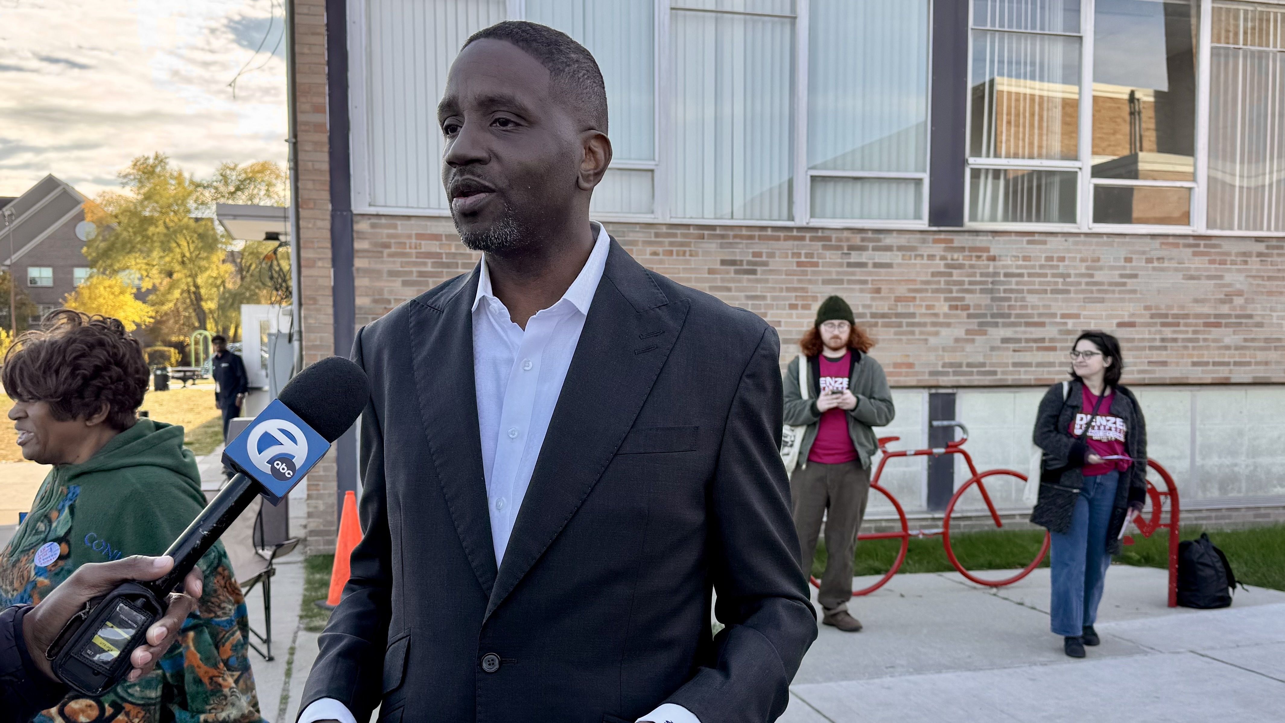 The Rev. Solomon Kinloch speaks to an interviewer holding a microphone on Election Day outside of a building. 