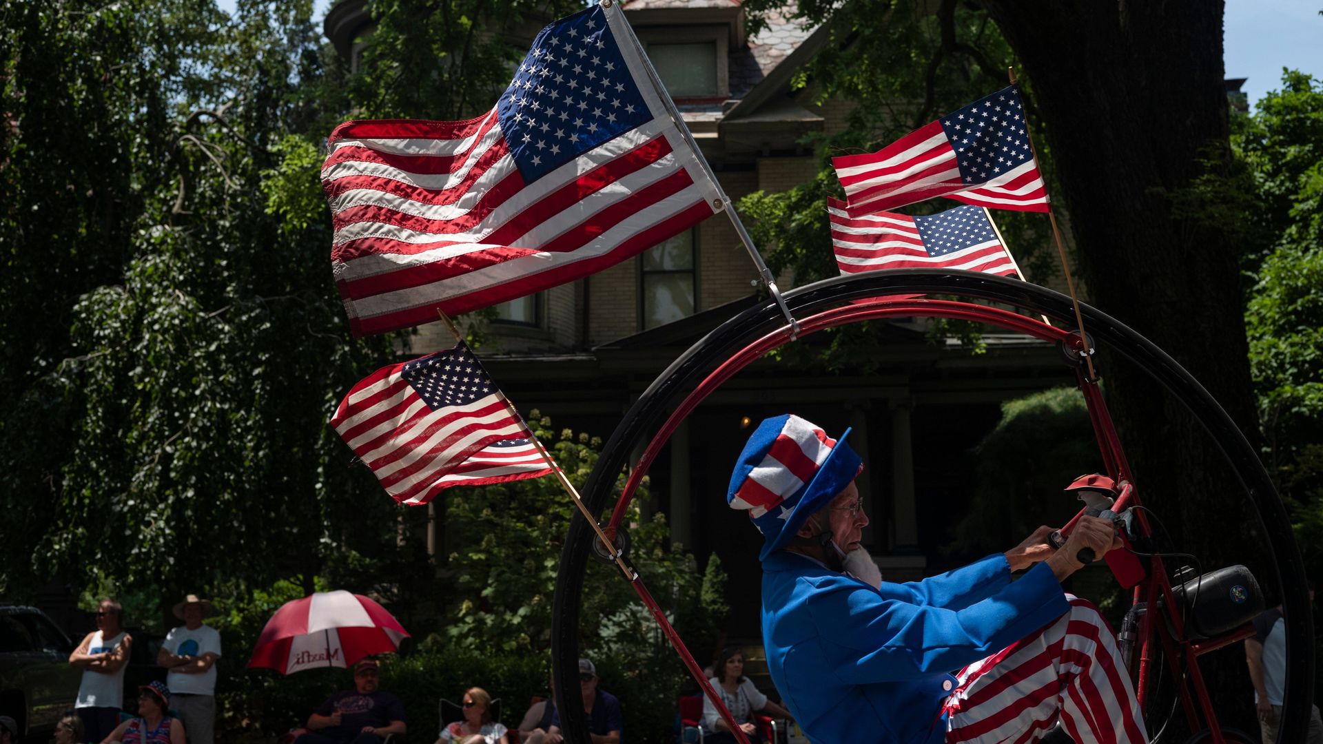 A man dressed as Uncle Sam rides a flag-adorned bicycle in a parade.