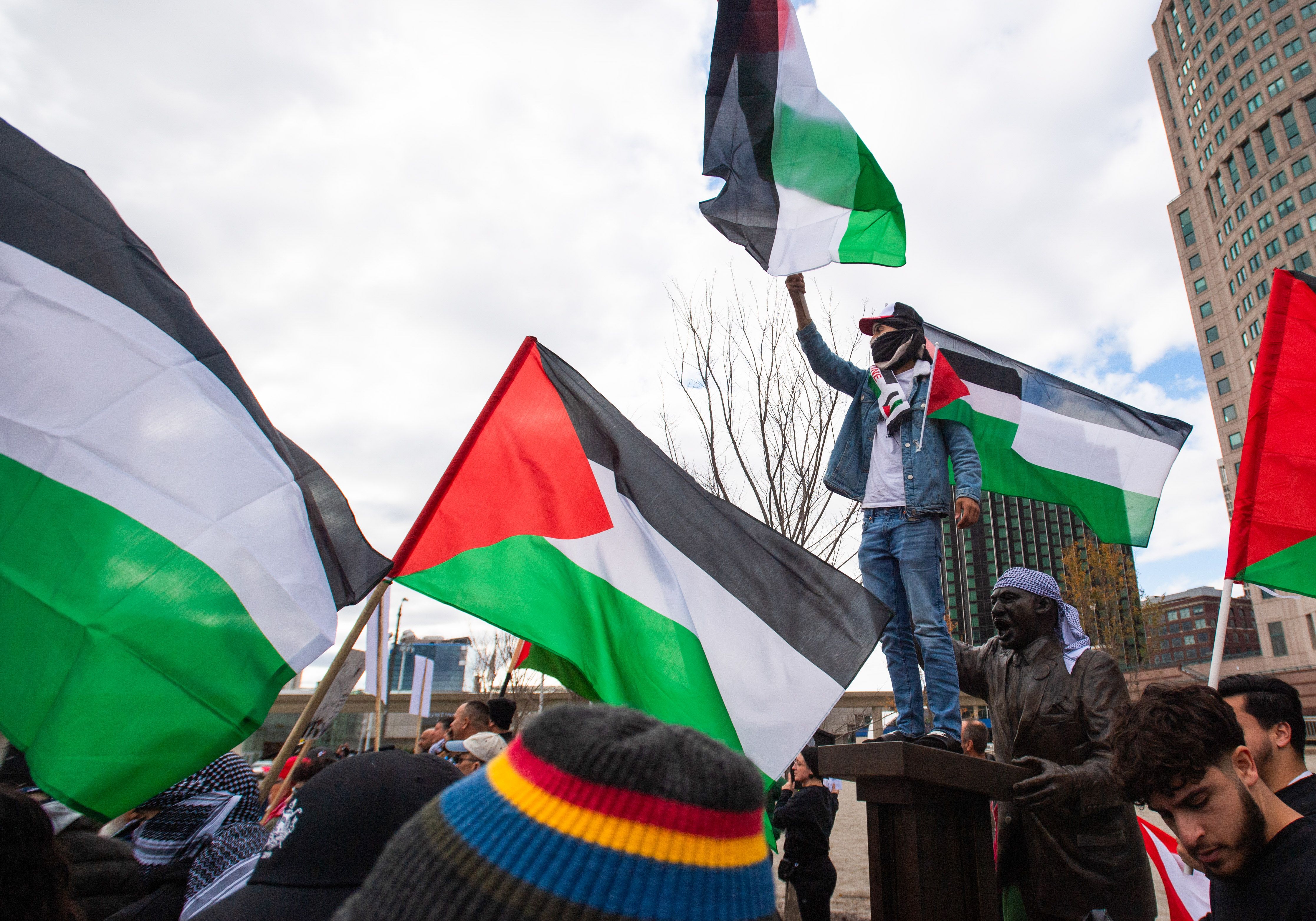 A protester waving a Palestinian Flag stands atop a statue of Martin Luther King Jr. during the demonstration in Detroit. 