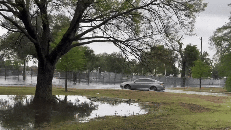 A car drives through a flooded street, sending up a spray of water.