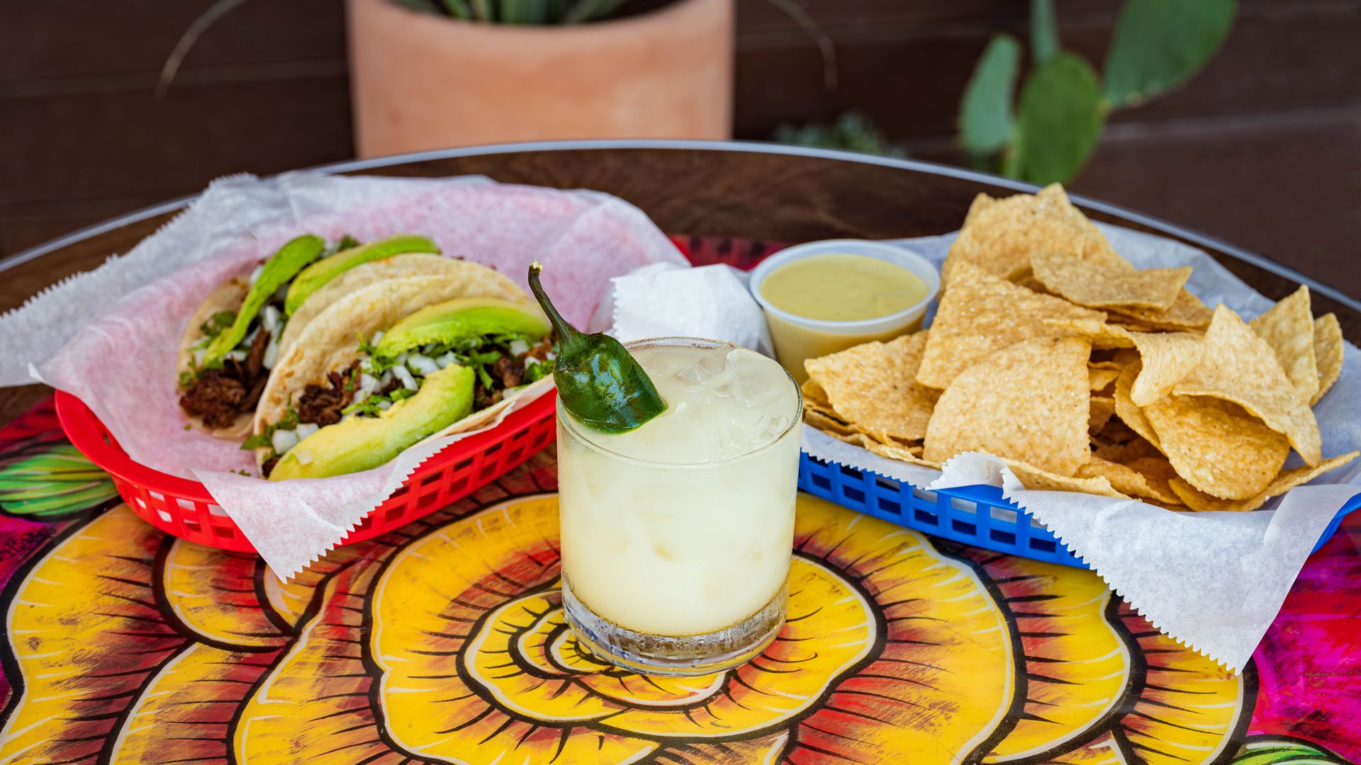 A photo of a margarita on a yellow table surrounded by chips and tacos.