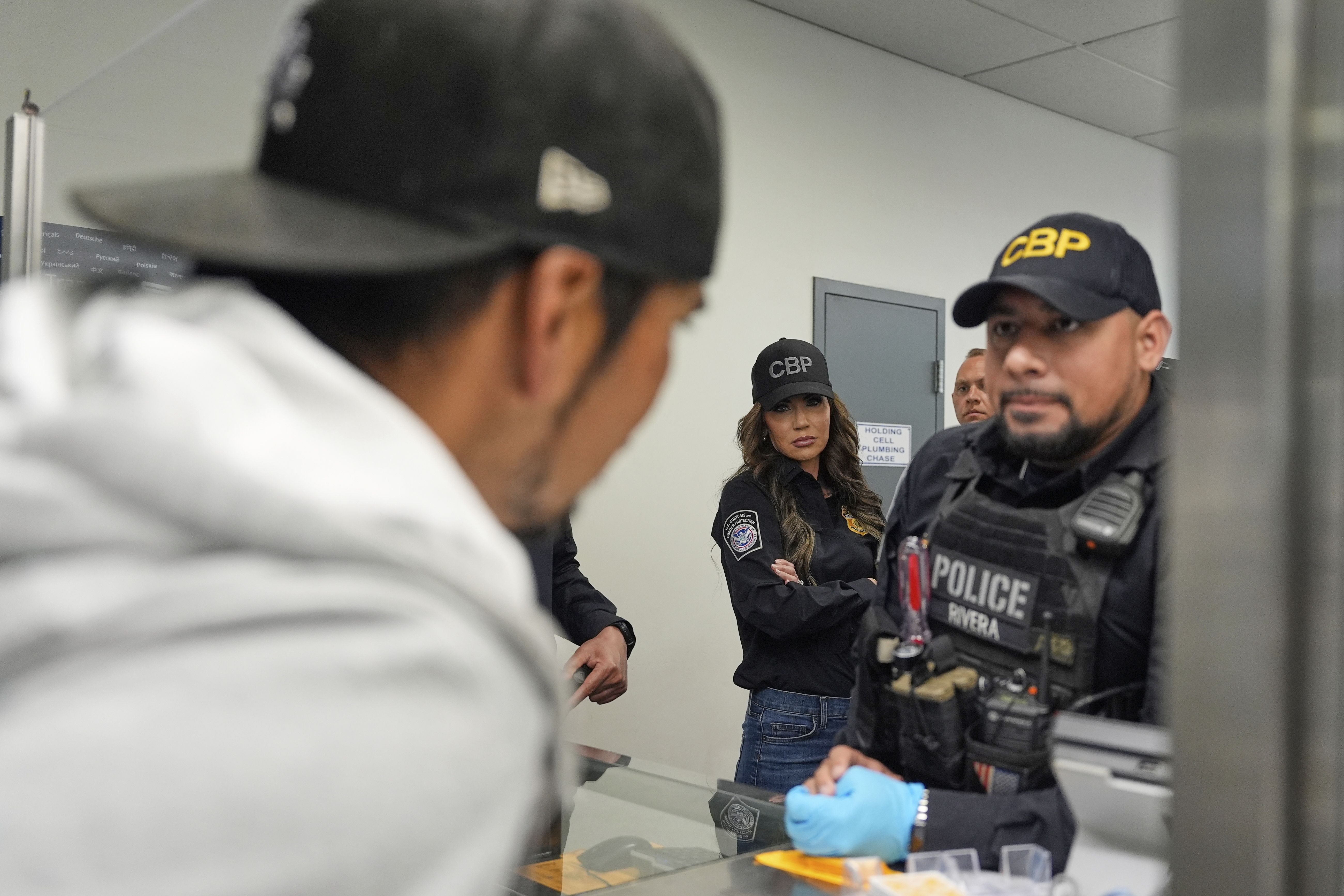 Homeland Security Secretary Kristi Noem, center, watches as officers speak with a person passing through the San Ysidro Port of Entry, Sunday, March 16, 2025, in San Diego. (AP Photo/Alex Brandon)