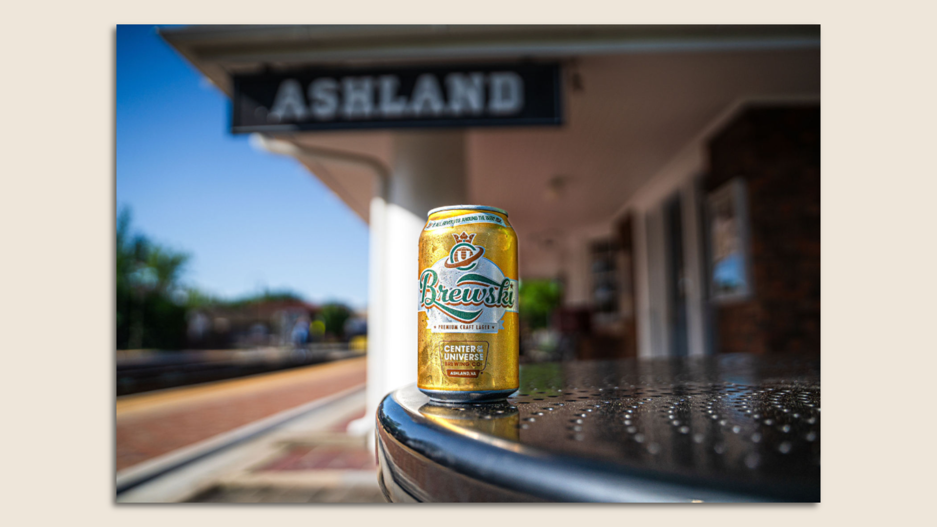 a can of beer called Brewski nest to a train track and under an Ashland sign