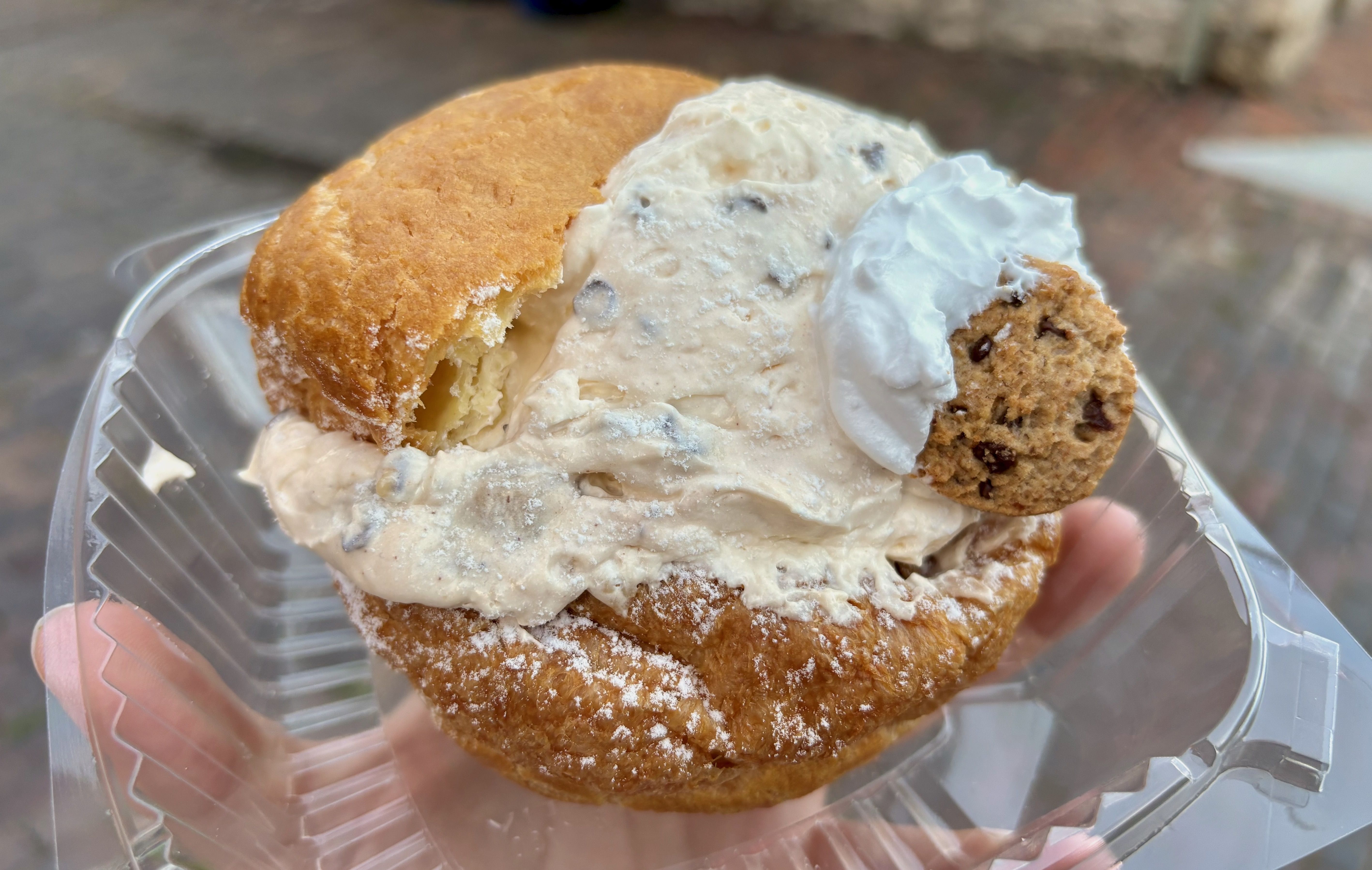 A close-up of a cookie dough cream puff, with creamy filling and topped with a chocolate chip cookie