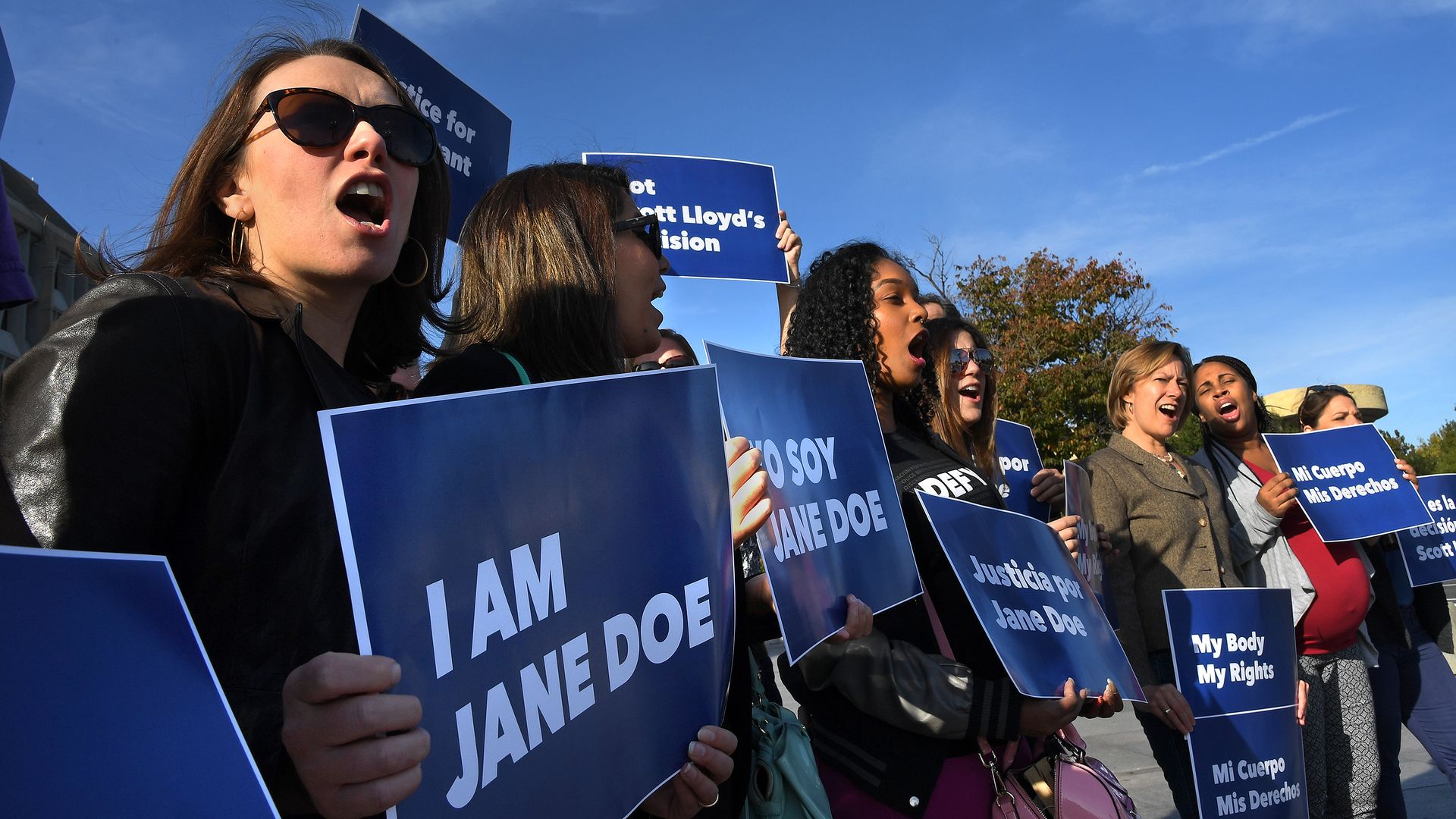 Women protesting with blue signs that say "I AM JANE DOE" 