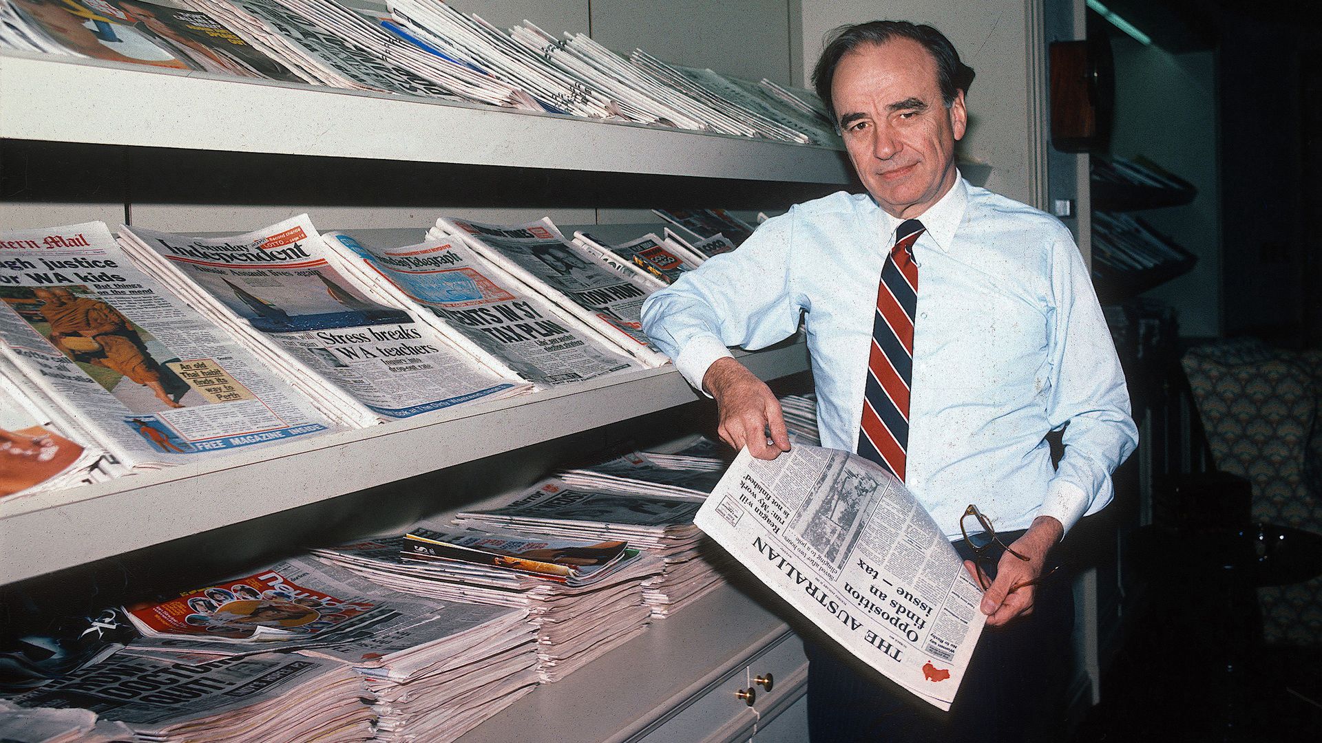 Portrait of Australian-born American media executive Rupert Murdoch as he poses, beside a display rack of periodicals he owns, in his office at the New York Post.