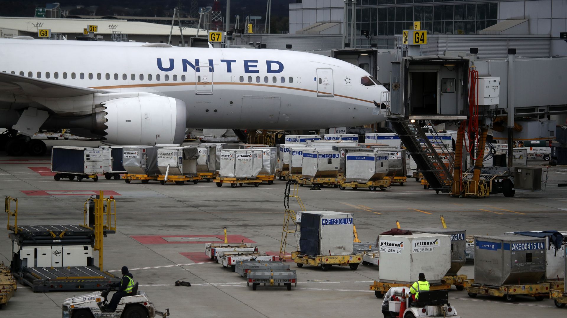 A United airplane sits at a gate surrounded by baggage carts
