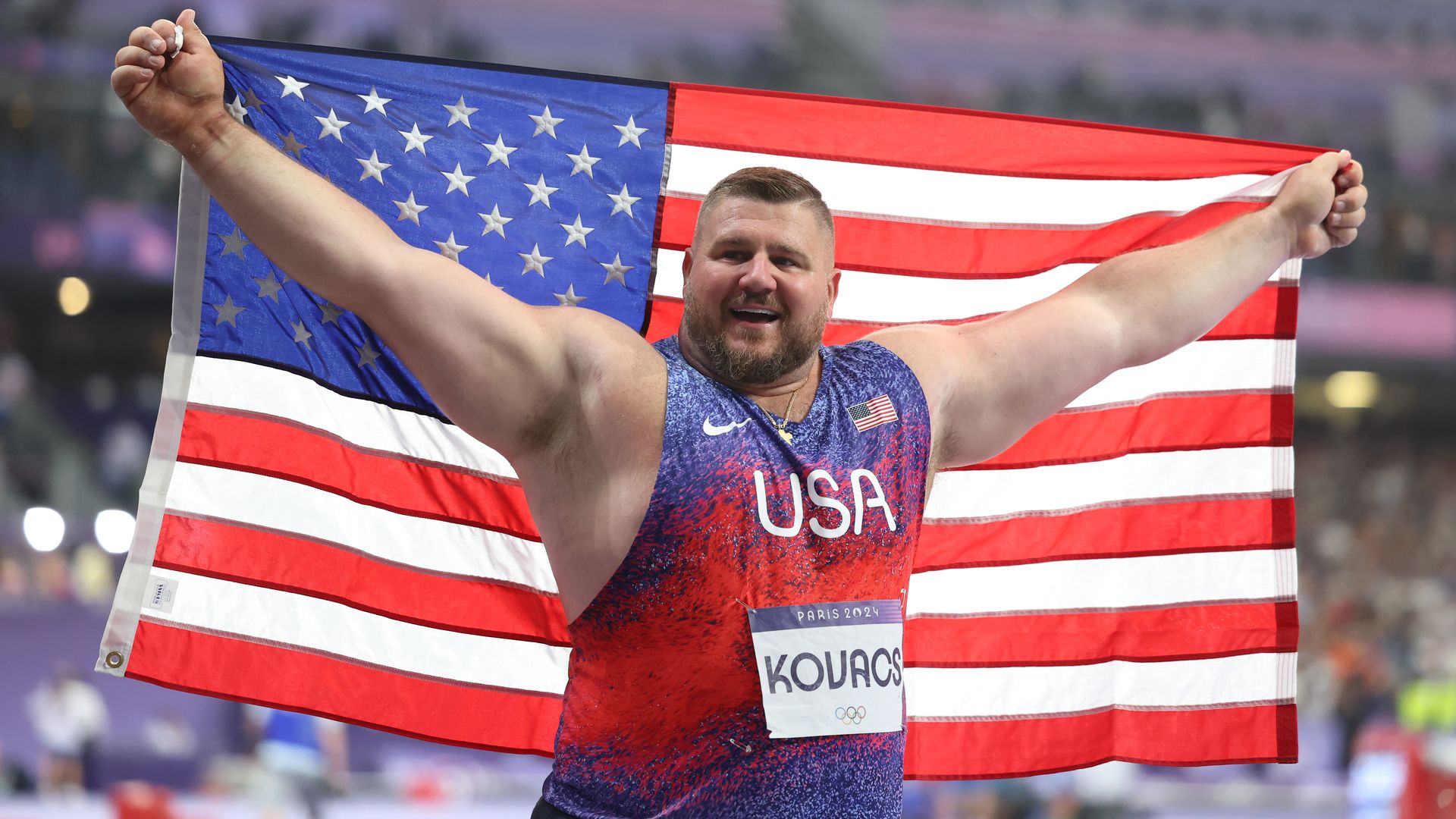 Shotput silver medalist Joe Kovacs holds an outstretched American flag. 