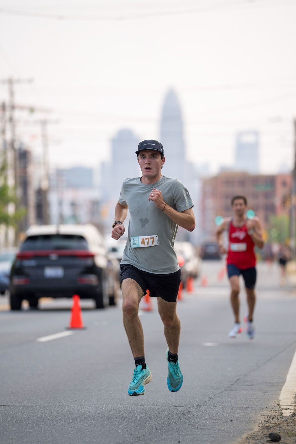 Runner in a grey shirt, navy blue hat and grey shorts strides forward. 