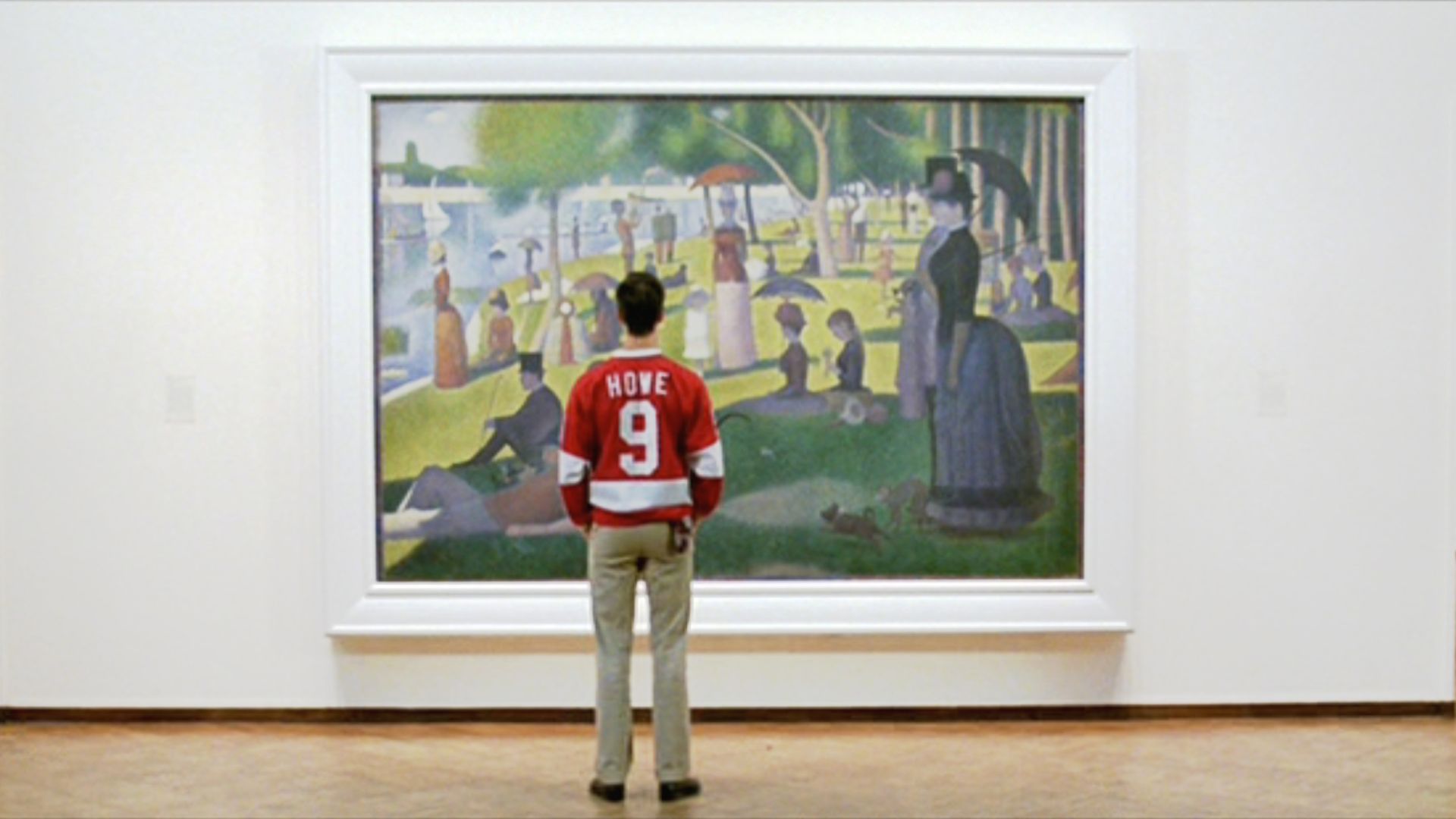 Back view of a man in a red HOWE jersey standing before a large painting in a white frame, depicting a sunny park with people, trees, a statue, and water in the background.
