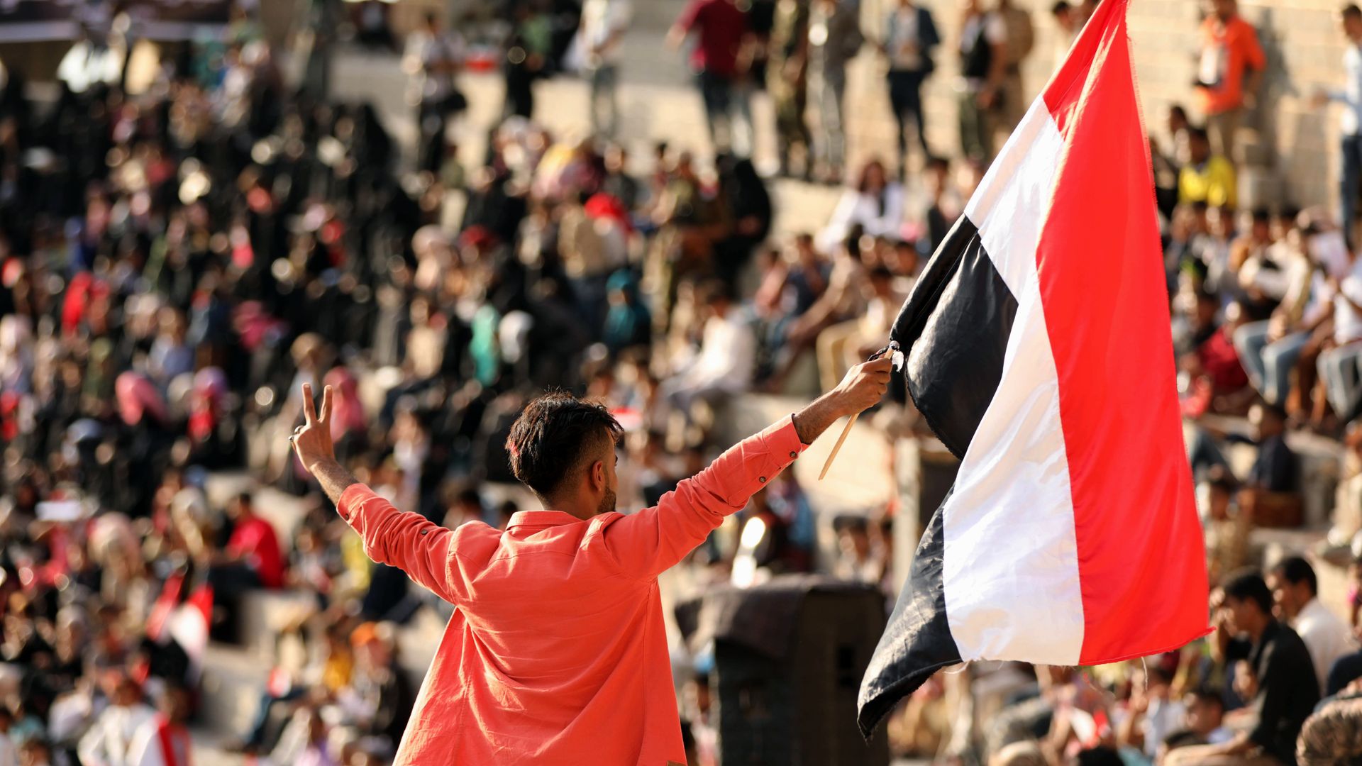A young person waves a Yemen flag in front of a crowd.