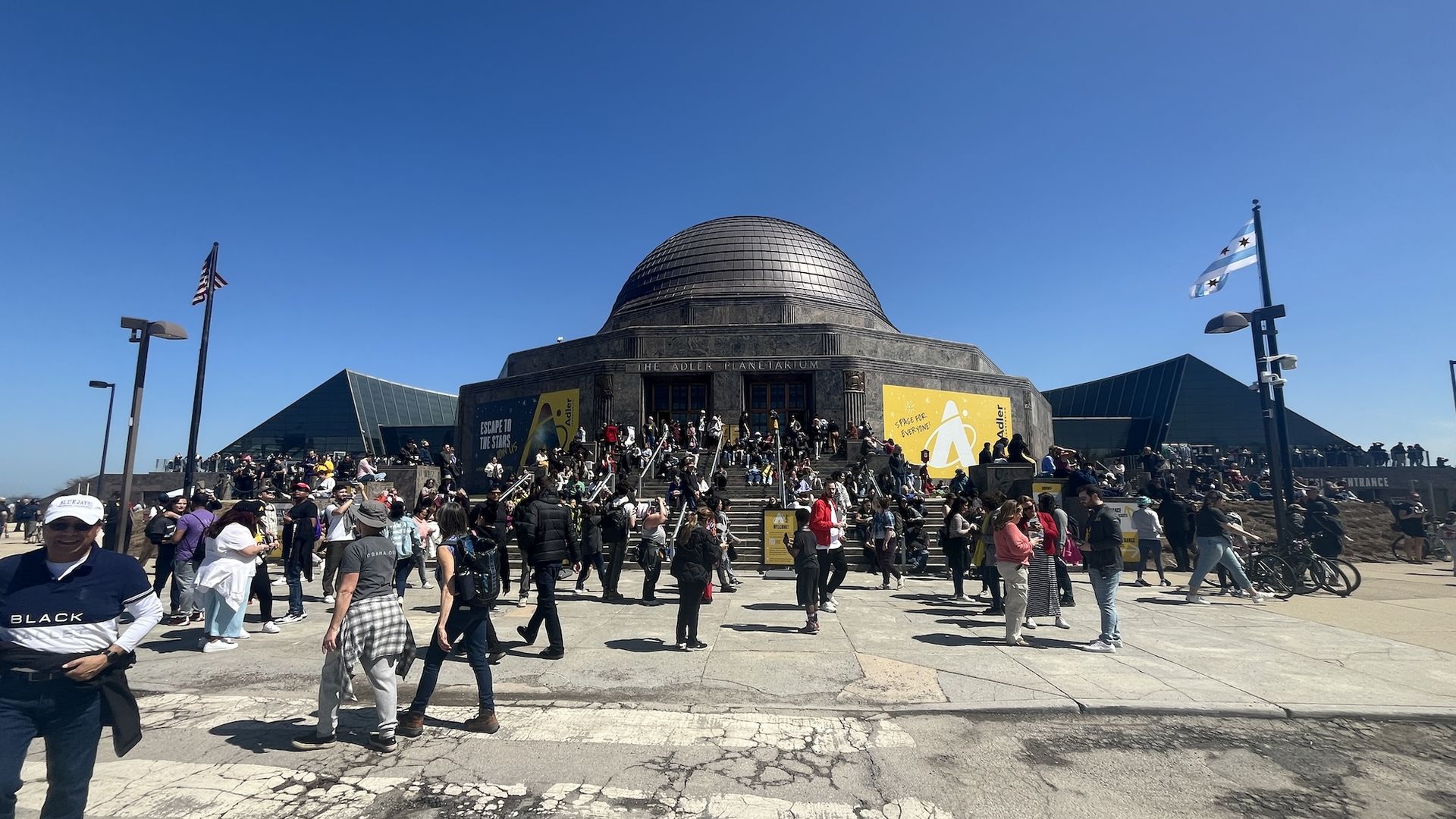 Adler Planetarium in front of blue sky with people walking around.