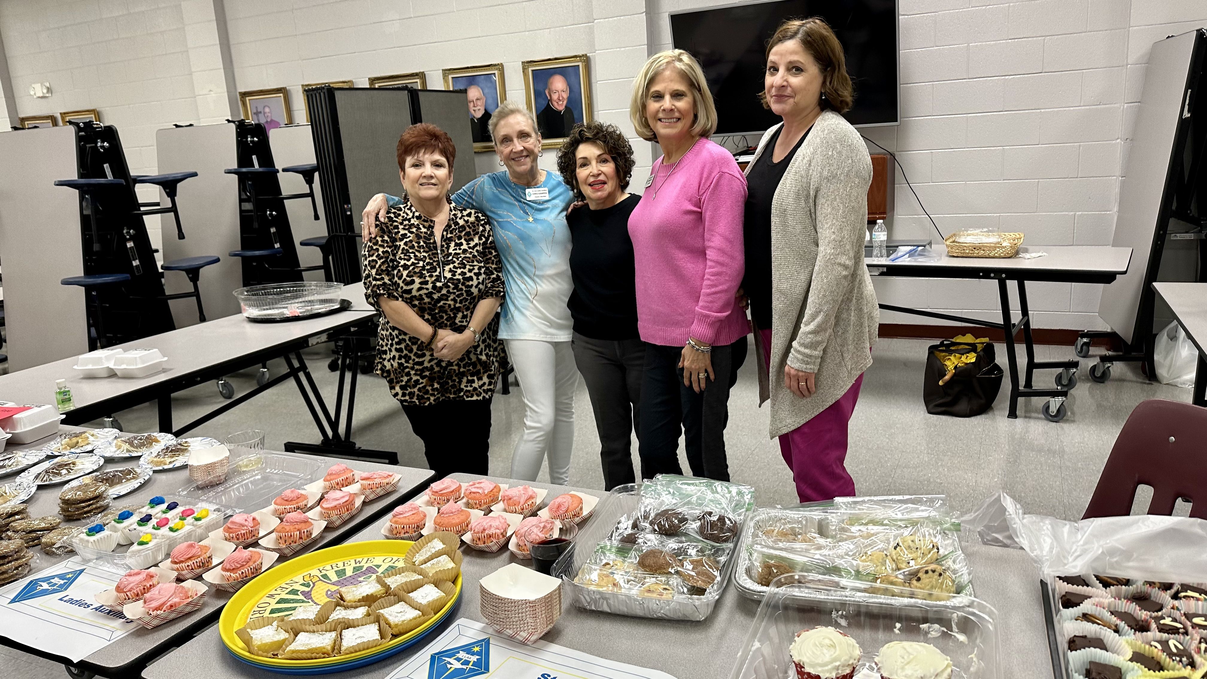 Photo shows five women standing behind tables laden with their homemade baked goods.