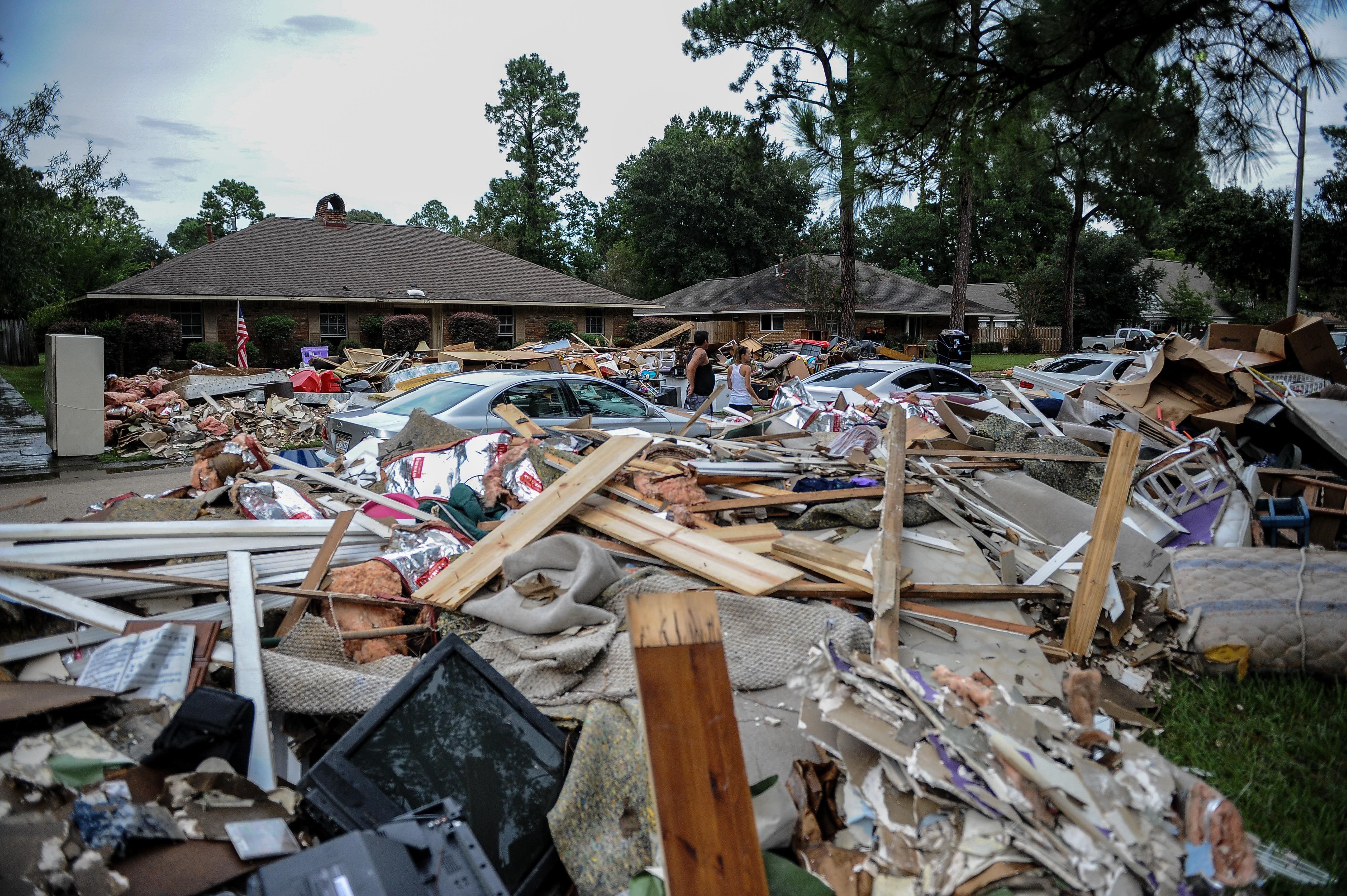 Photo shows boards and debris piled in font of homes and cars.