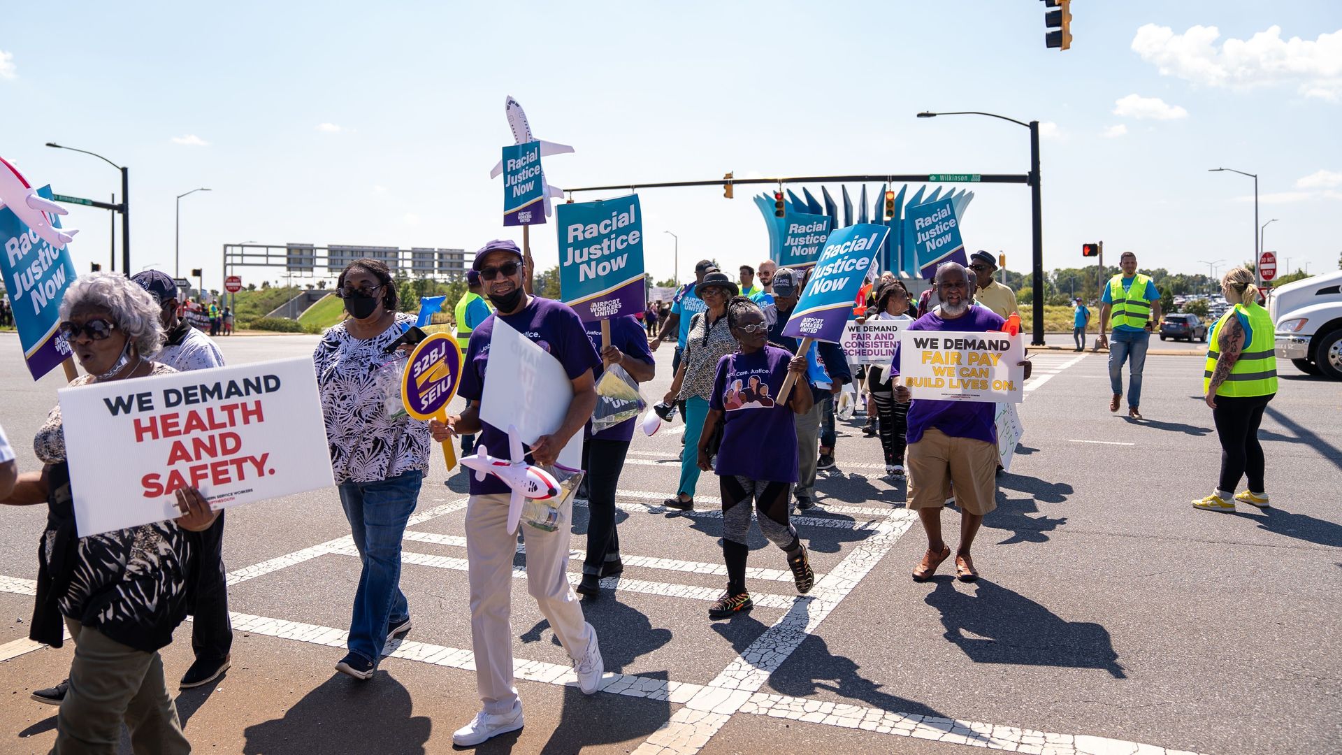 people walking across a crosswalk holding signs in protest of better wages