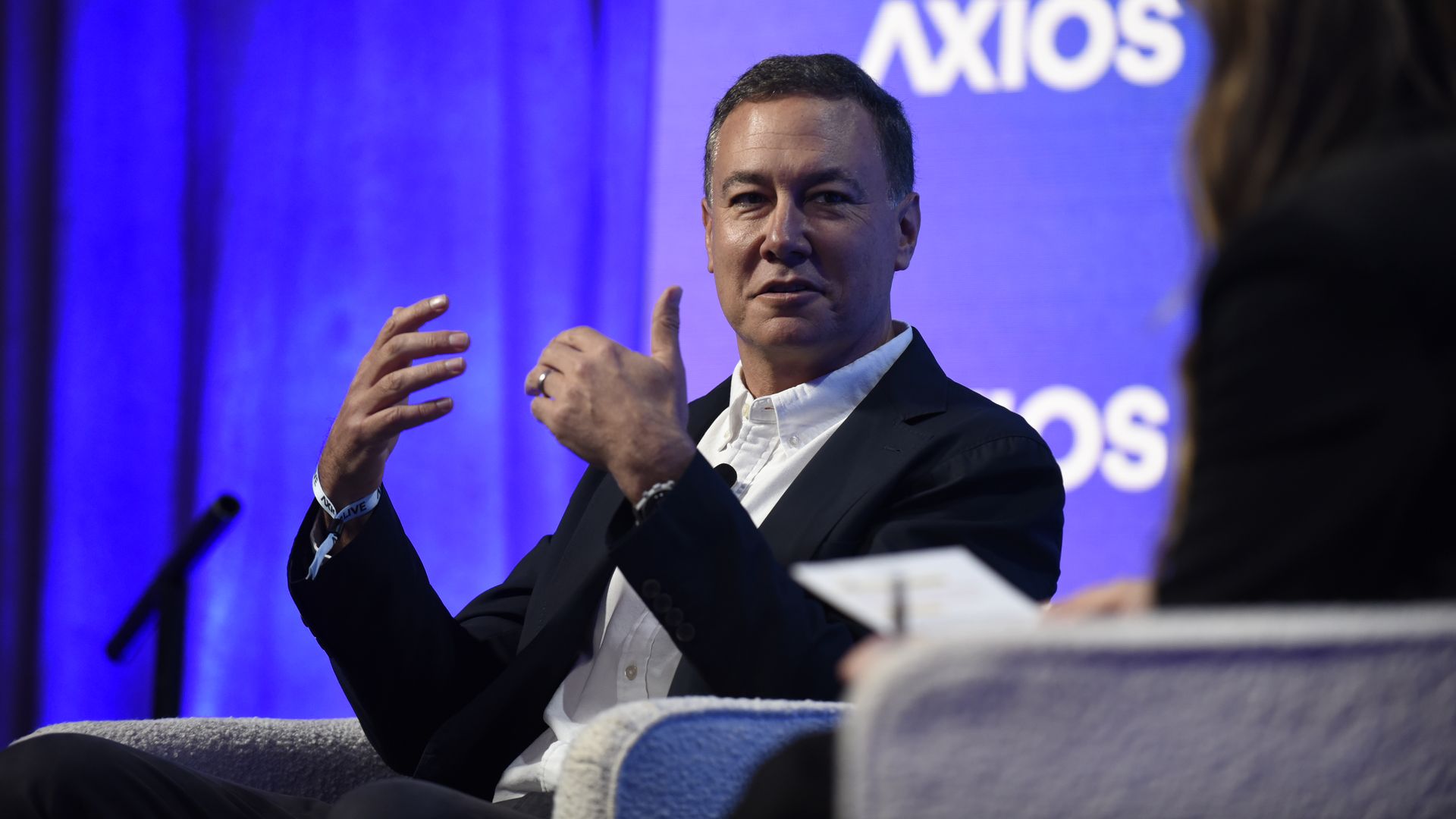 Yahoo CEO Jim Lanzone in a dark suit and white shirt gestures while speaking on a panel; a blue backdrop with the Axios logo is visible behind him.
