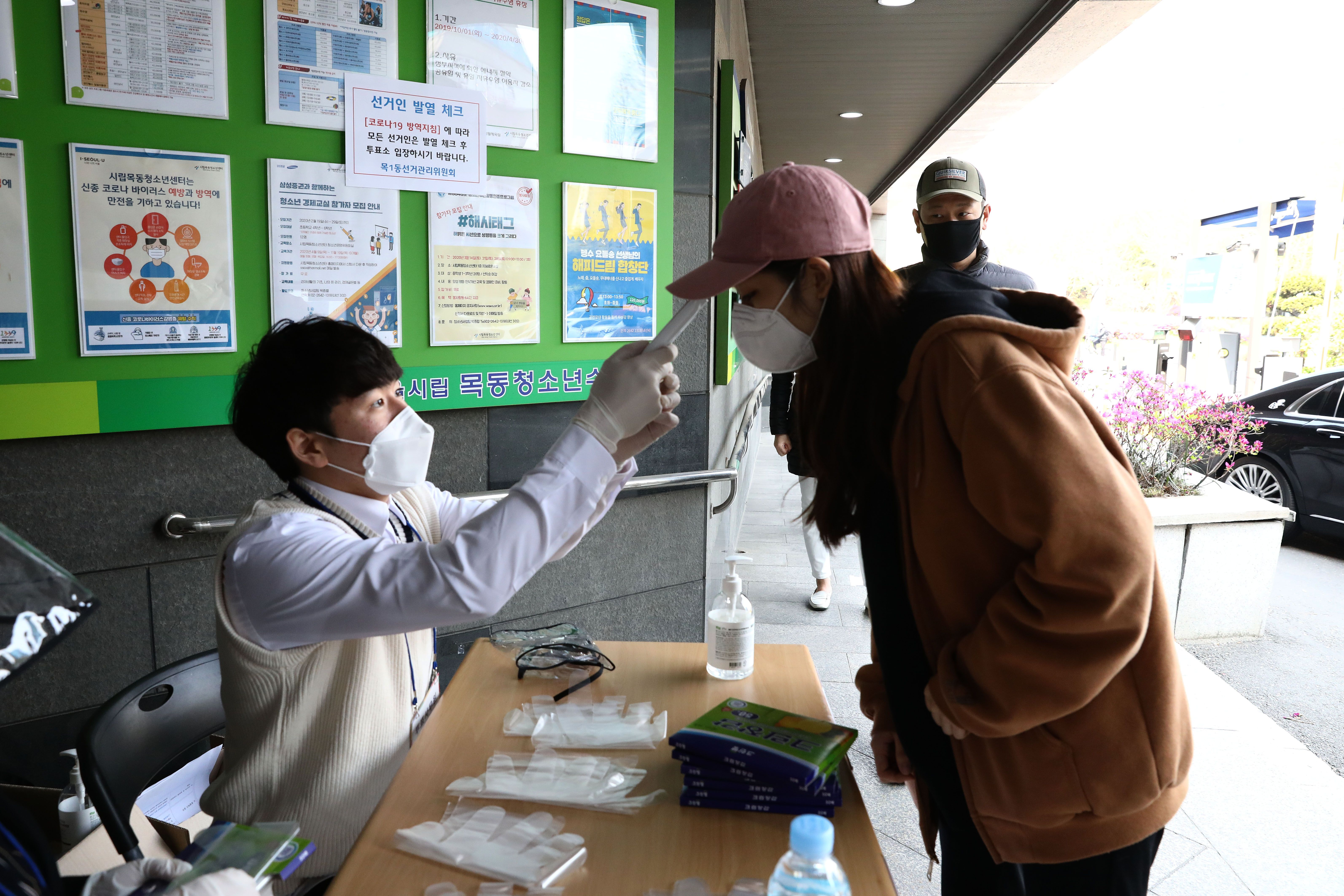 In this image, a woman has her temperature checked while waiting in line to vote 
