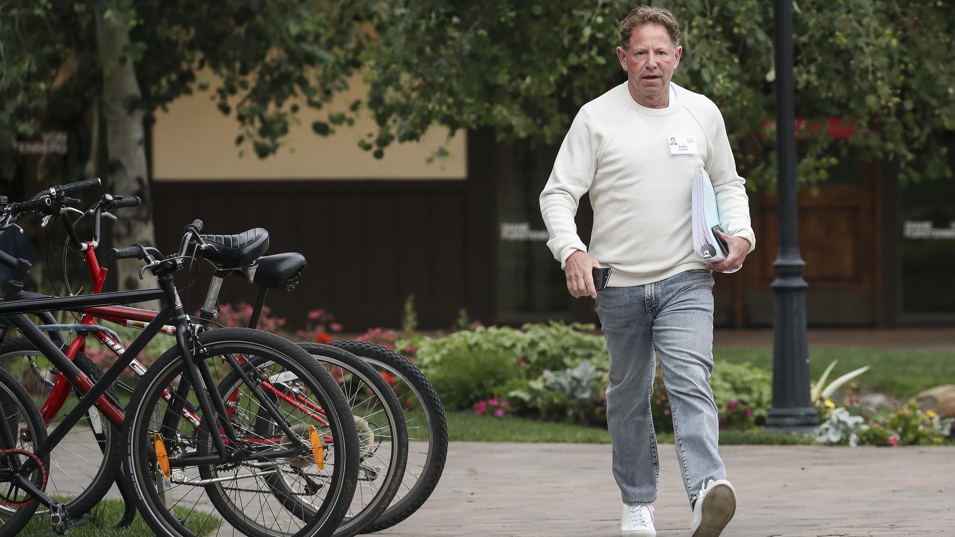 A man in a white shirt and jeans strolls on a sidewalk alongside a bike rack.