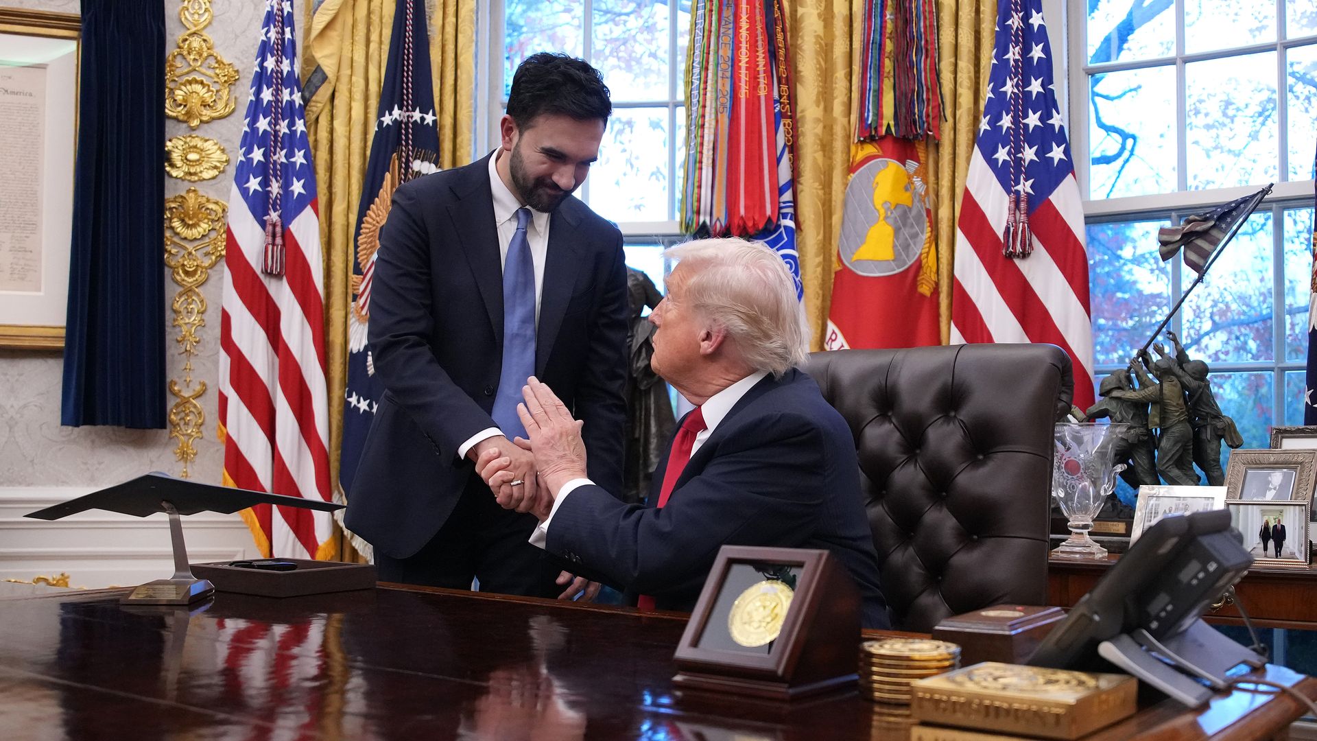President Trump, seated, and NYC mayor-elect Zohran Mamdani, standing, shake hands in the Oval Office. 