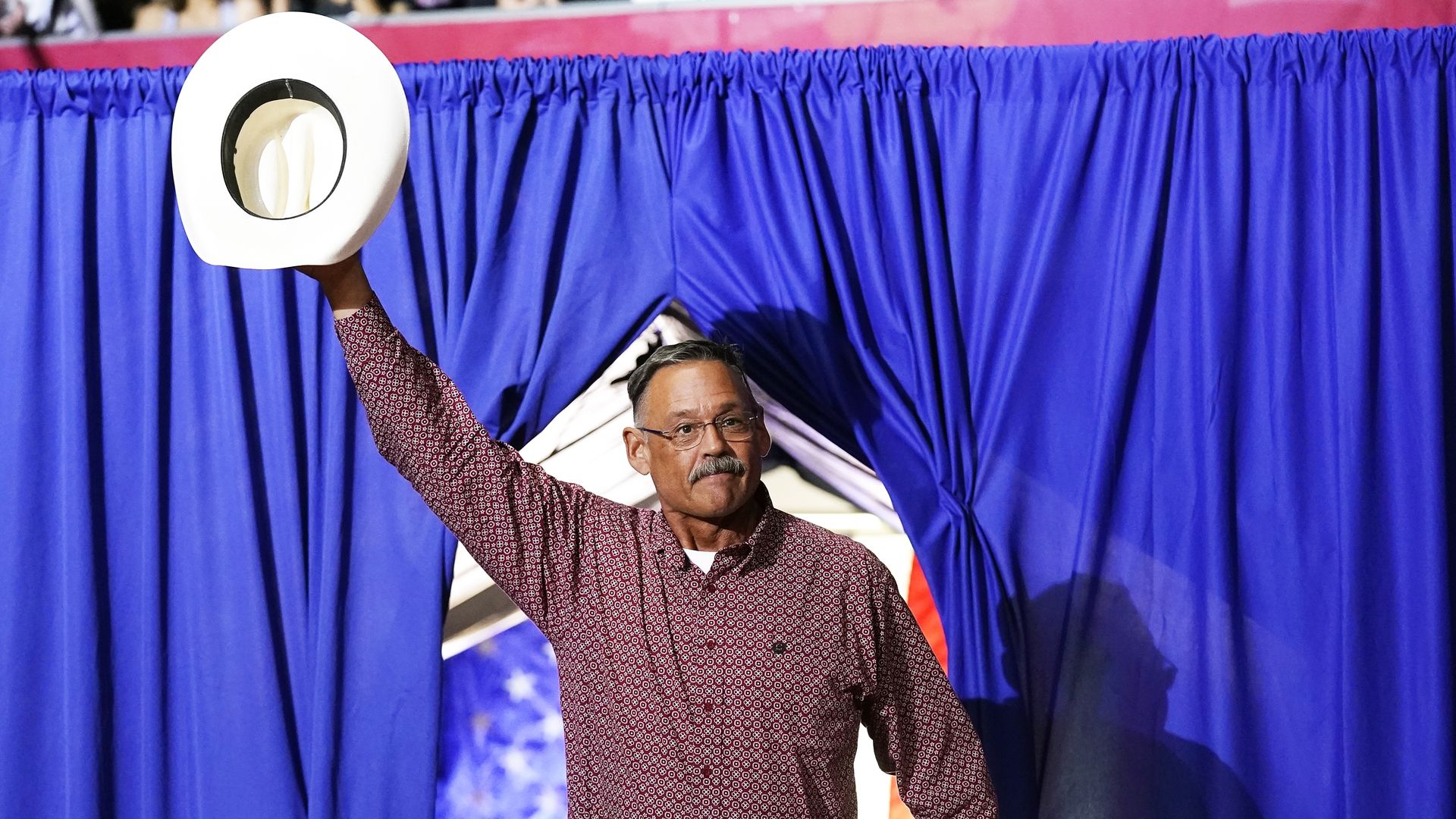 Mark Finchem waves a cowboy hat above his head on a stage