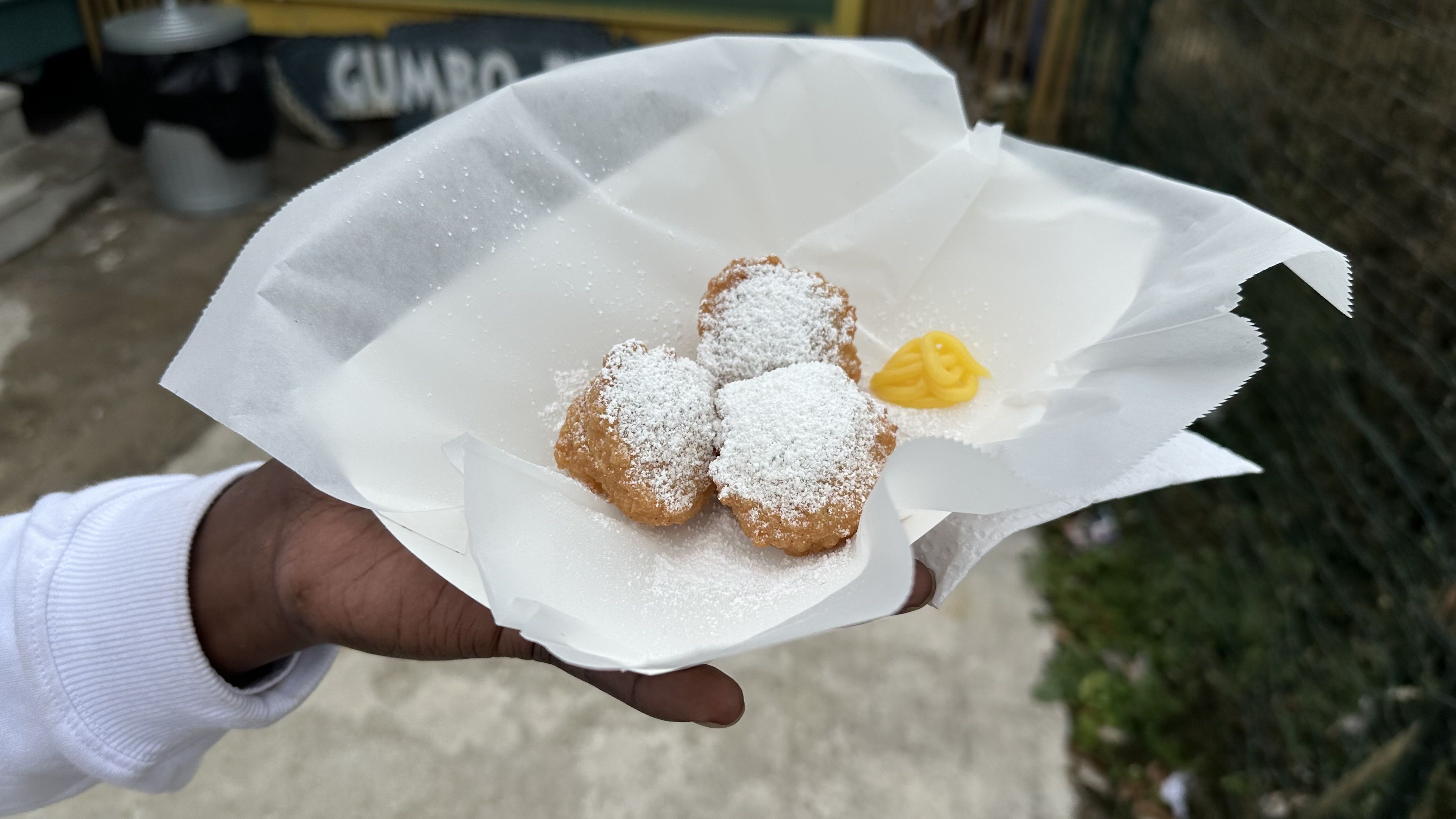 Brandan Pellerin holds a paper tray of calas, which are small Creole rice fritters. The plate of three of them is dusted with confectioner's sugar and served with a dollop of lemon curd. 