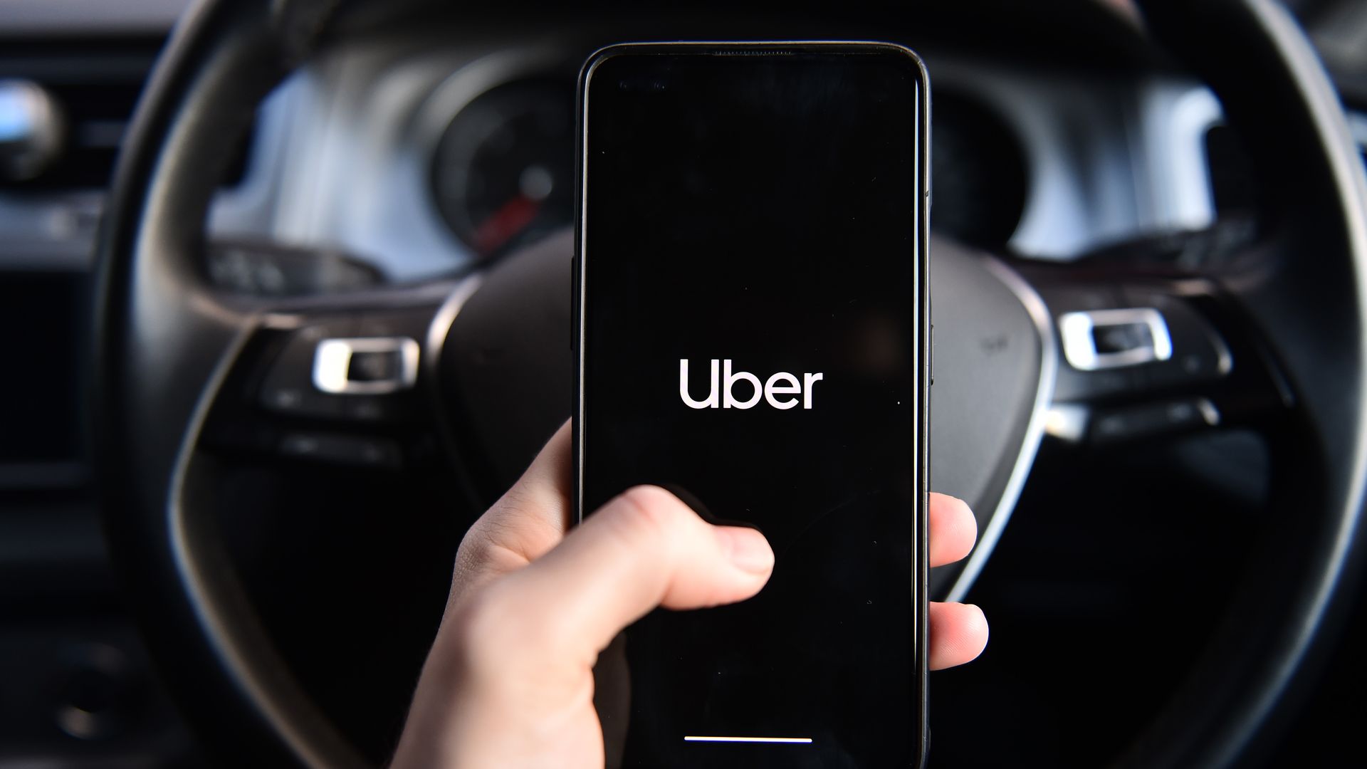hand holding uber phone in front of steering wheel