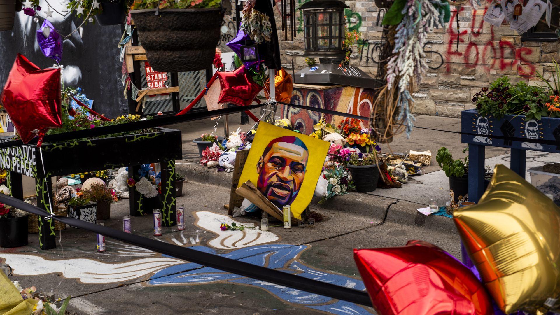 Photo of a memorial site dedicated to George Floyd with balloons, flowers and a portrait