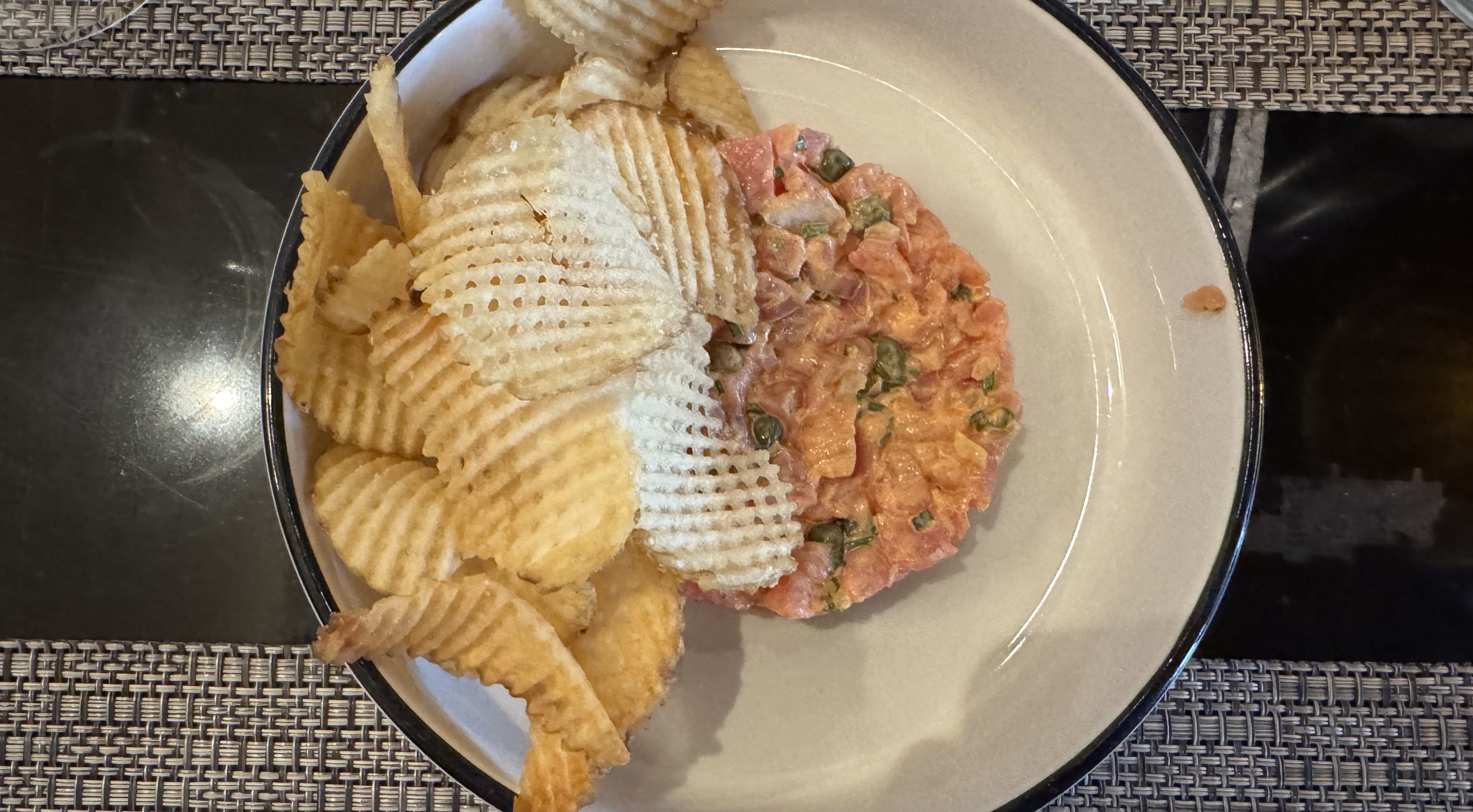 A bowl of blue fin tuna tartare topped with ridged potato chips sits on a restaurant table.